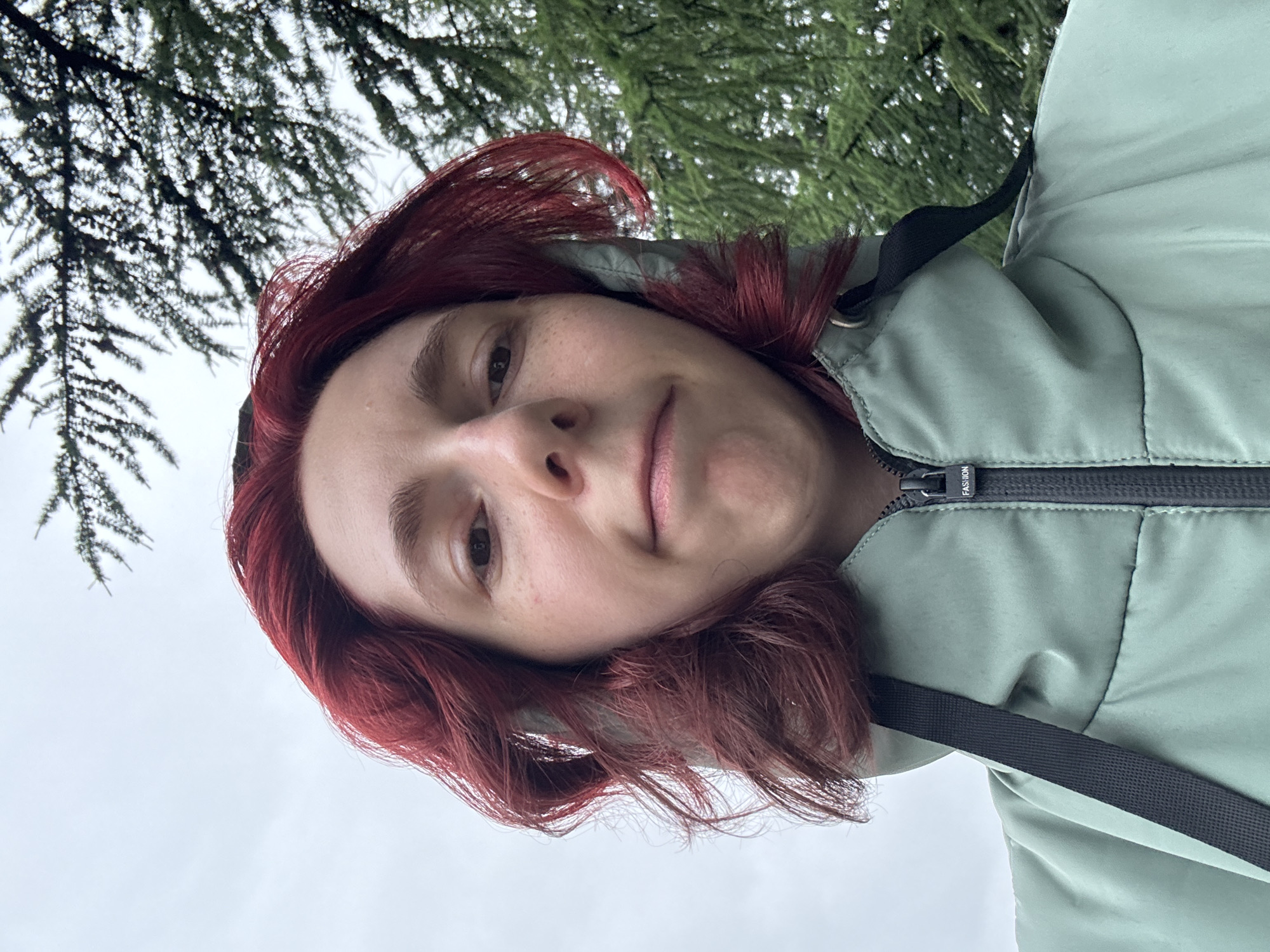 Red-haired figure in green hoodie, urban outdoor selfies