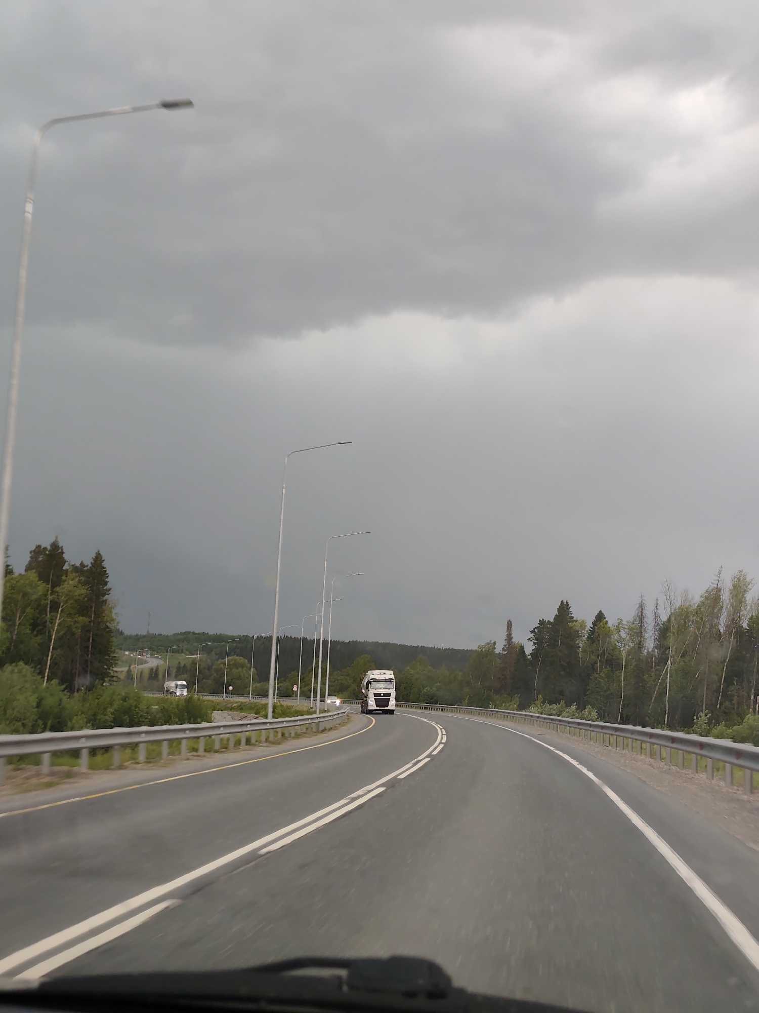 White truck travels forest road in Chusovskoye under cloudy skies