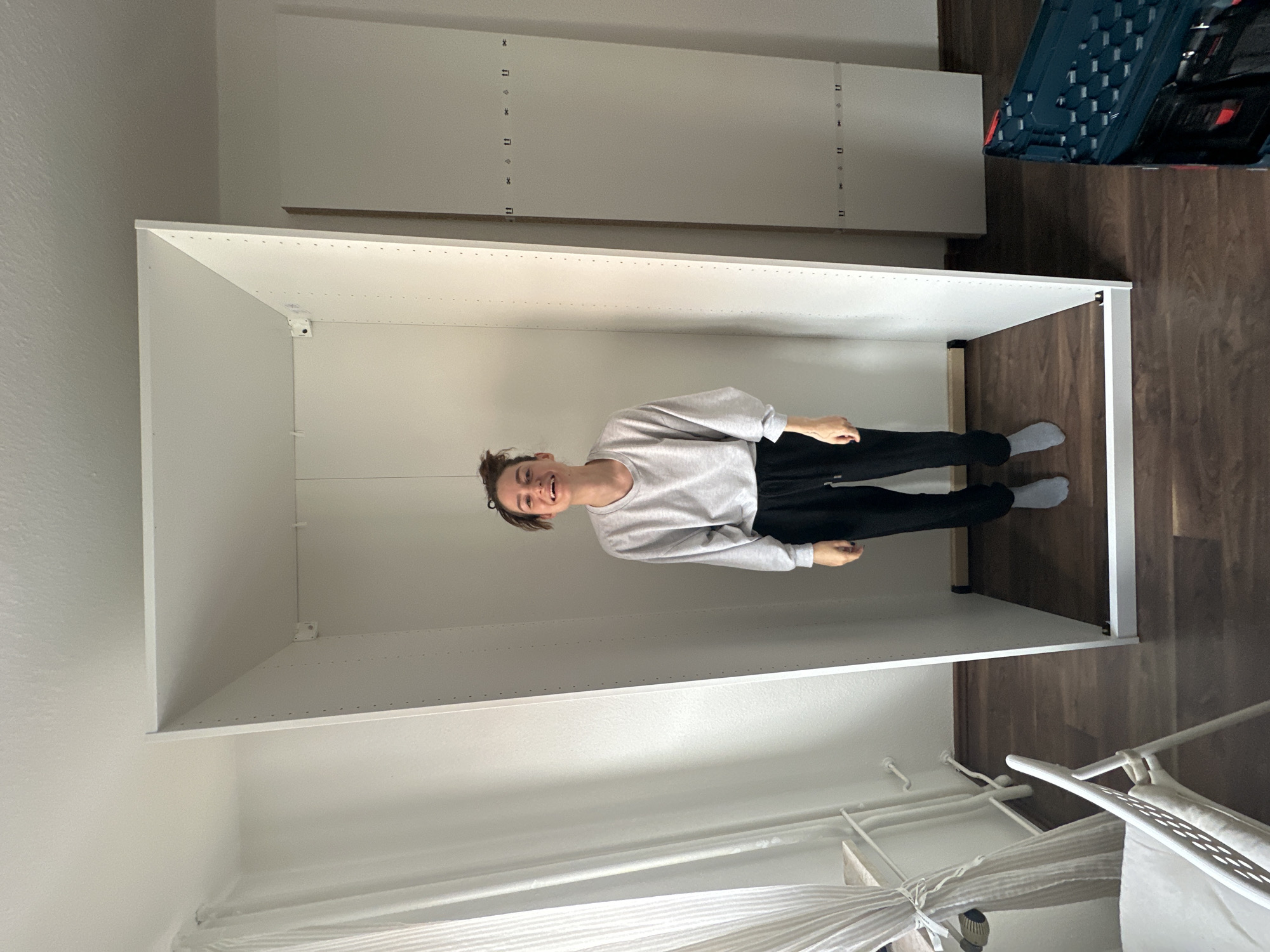 Woman poses playfully inside wardrobe frame during furniture assembly
