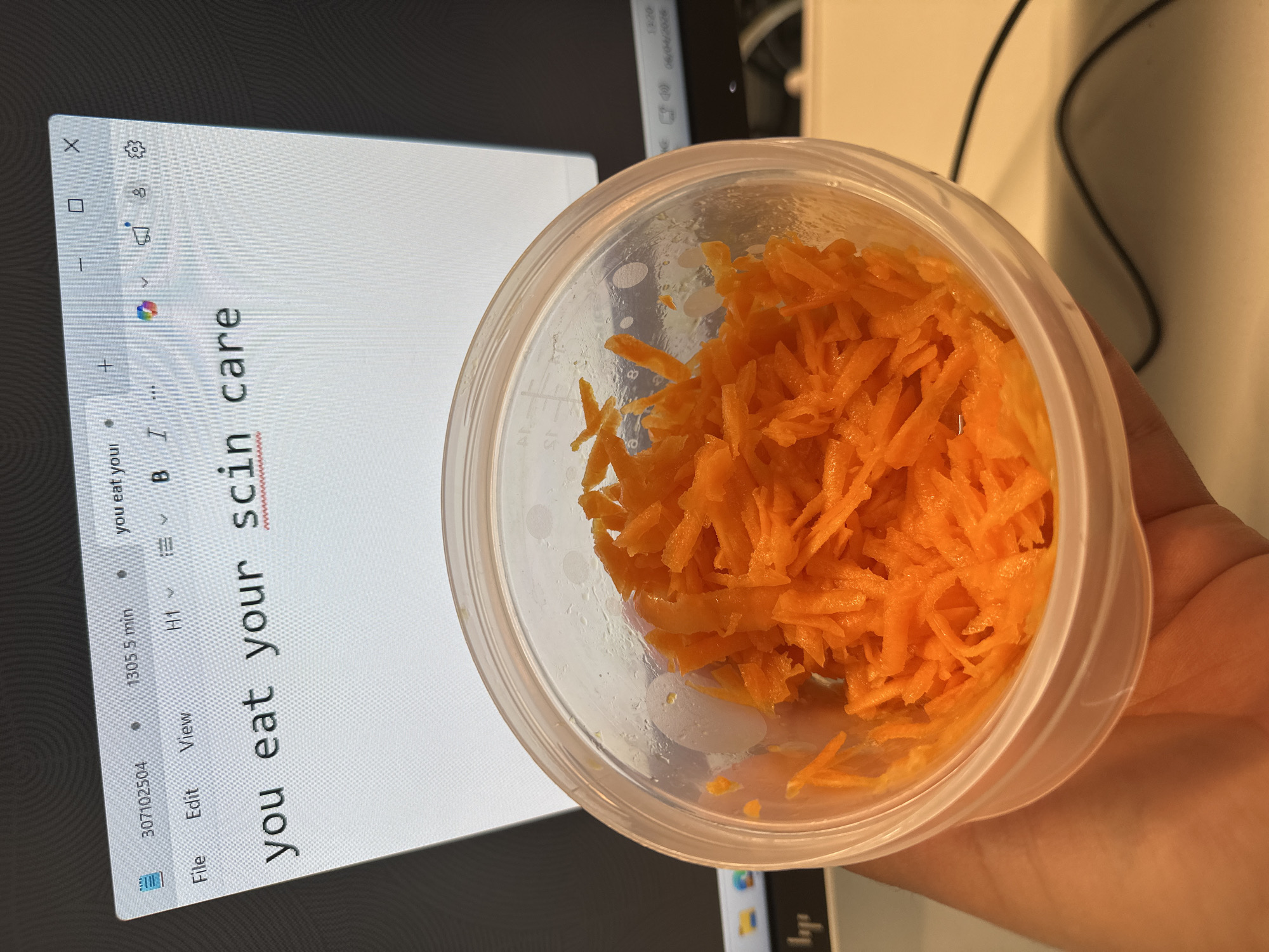 Person holds shredded carrots near computer screen in Alicante