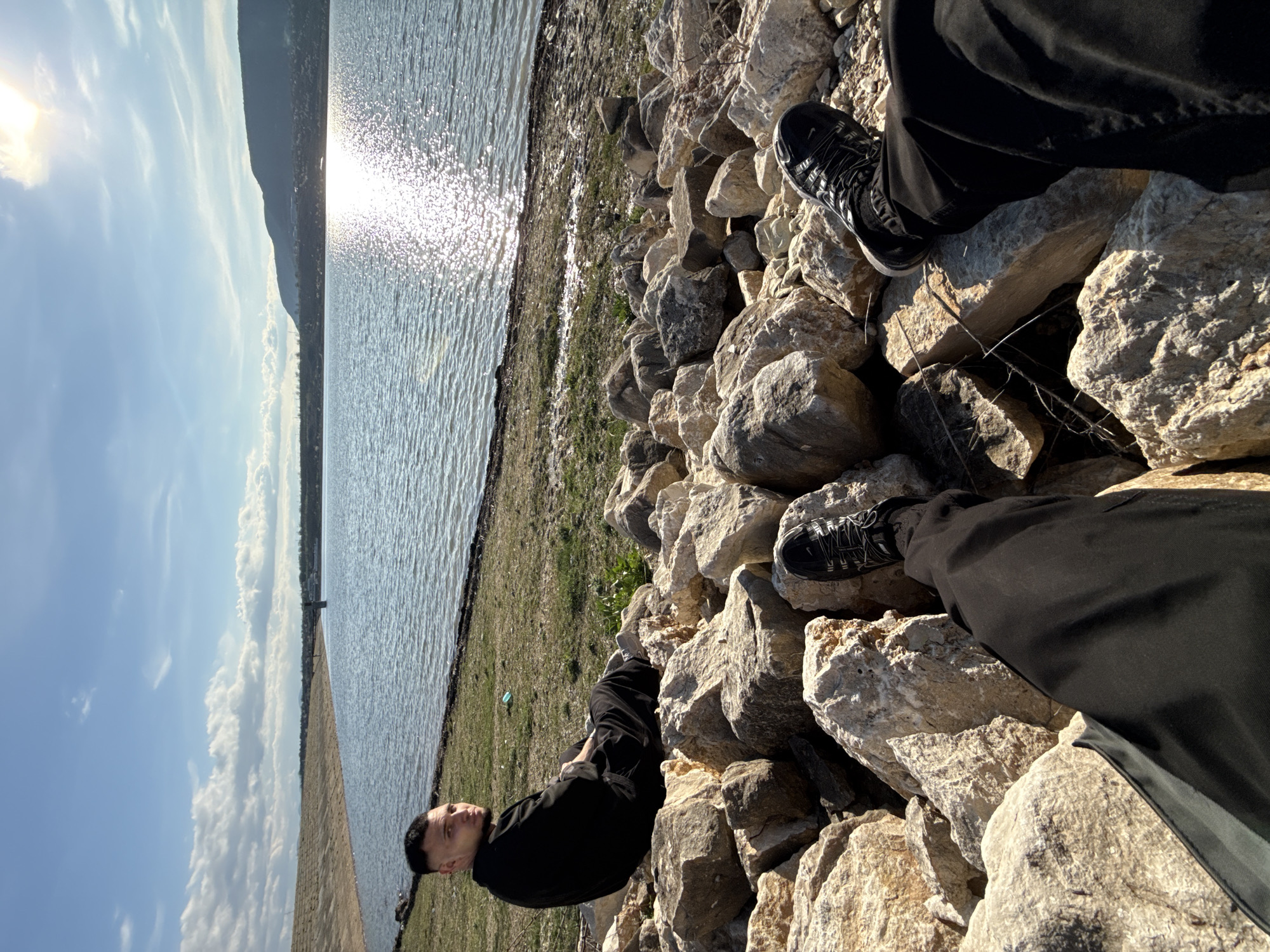 Person sits by water on rocky embankment in Shumen