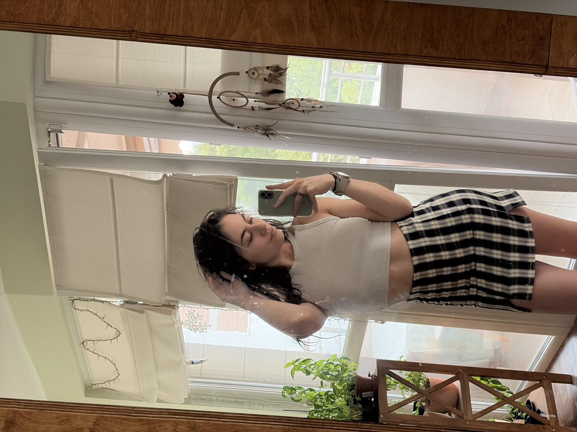 Mirror selfie in a bedroom, crop top and plaid skirt.