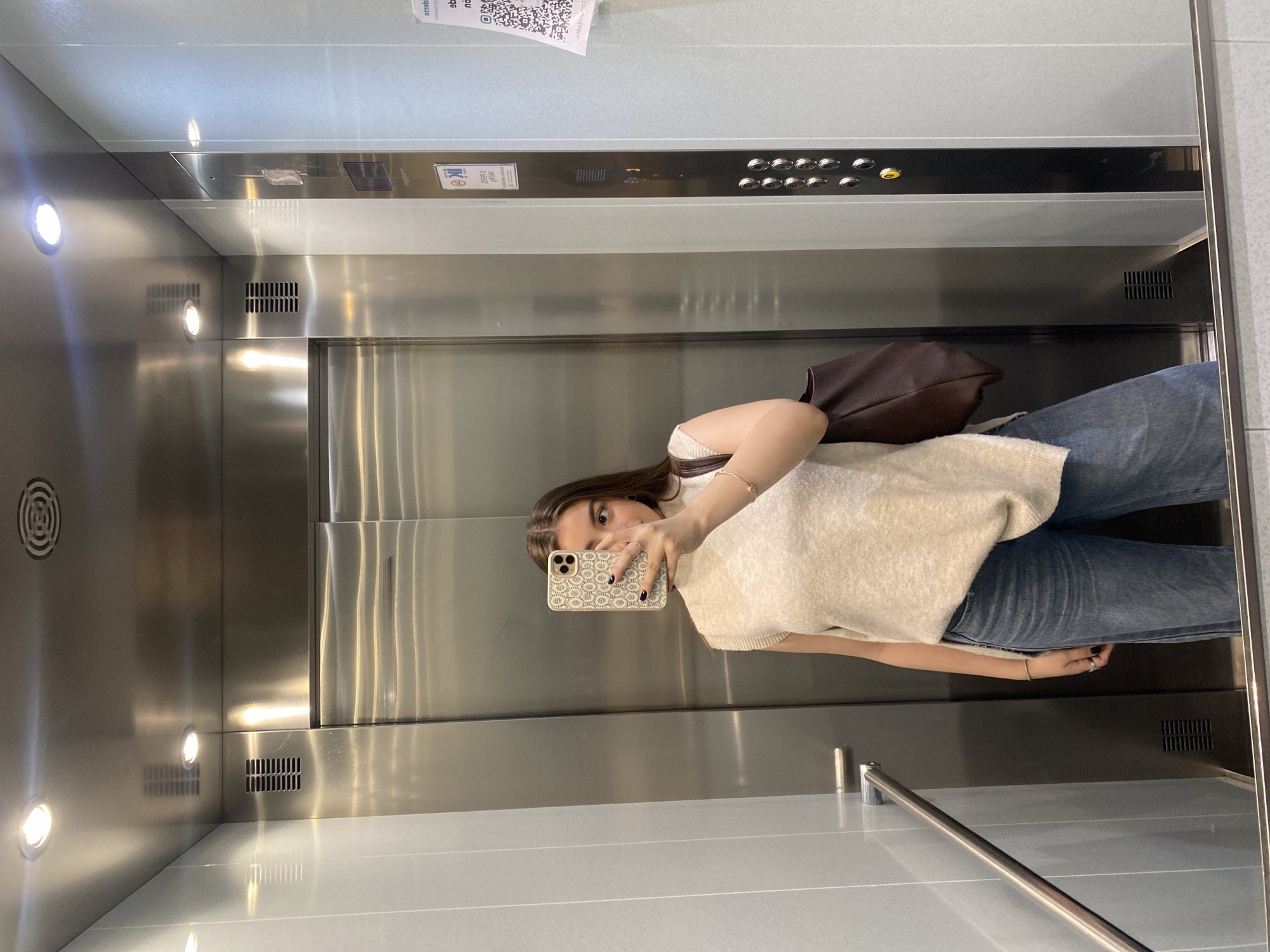 Woman takes mirror selfie in metal elevator