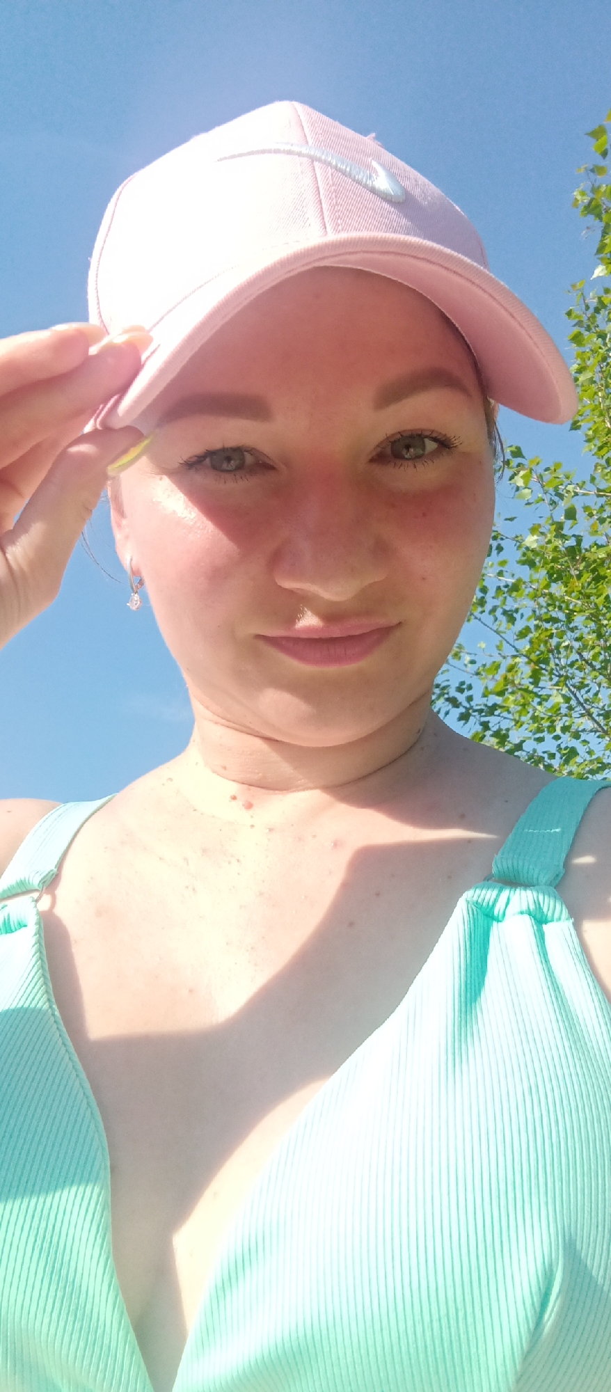 Woman poses for sunlit selfie in swimsuit and baseball cap