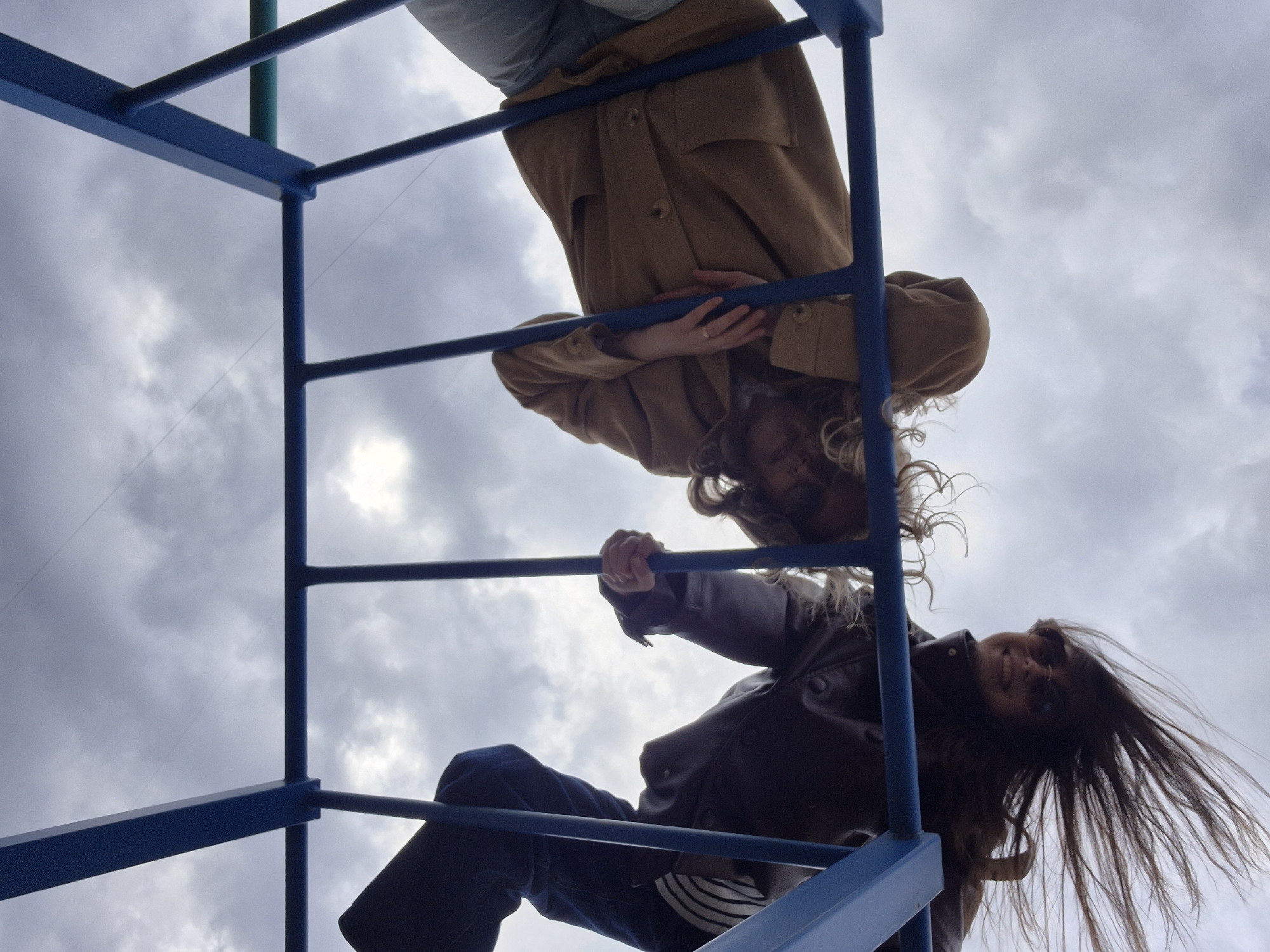 Young adults hang upside down from playground climbing frame