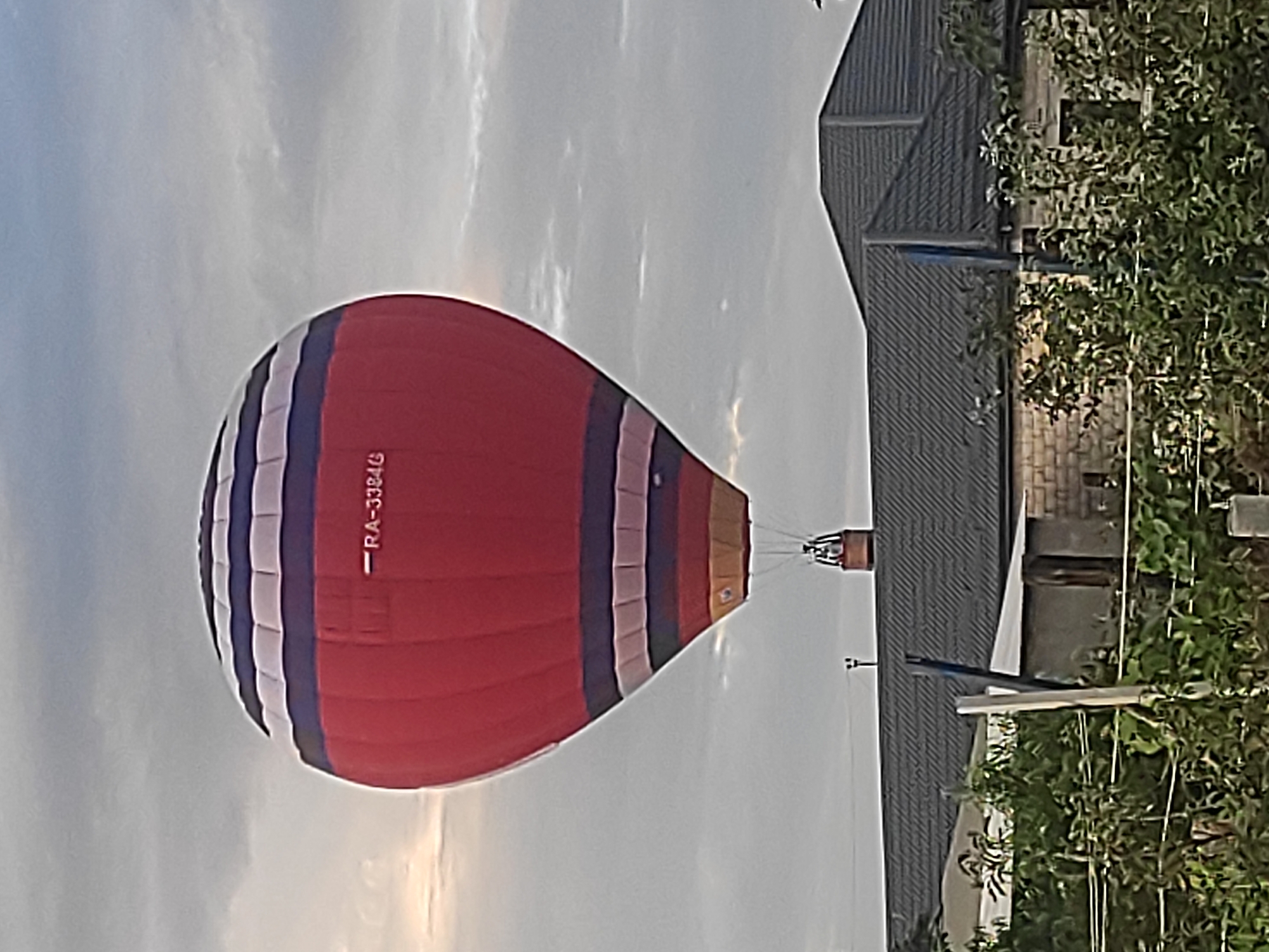 Striped hot air balloon RA-3384G ascends over residential area