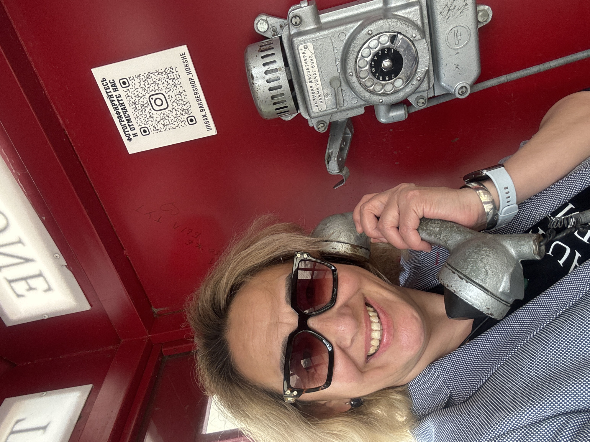 Woman uses vintage rotary phone in red booth, Kazakhstan