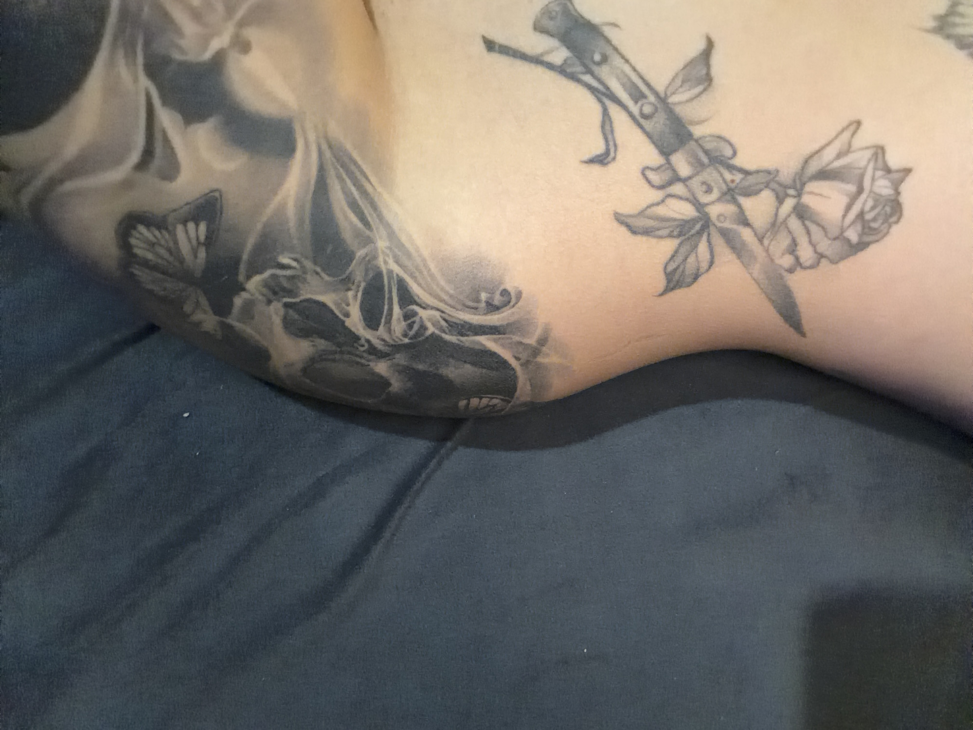 Person displays multiple black ink tattoos including skull butterfly rose