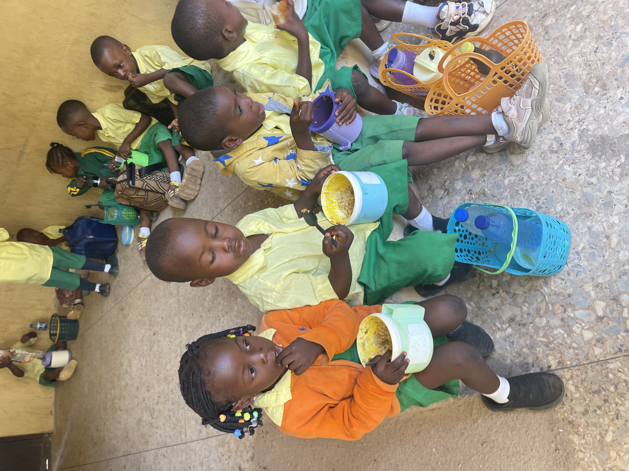 Schoolchildren eat lunch outdoors in Akwanga schoolyard