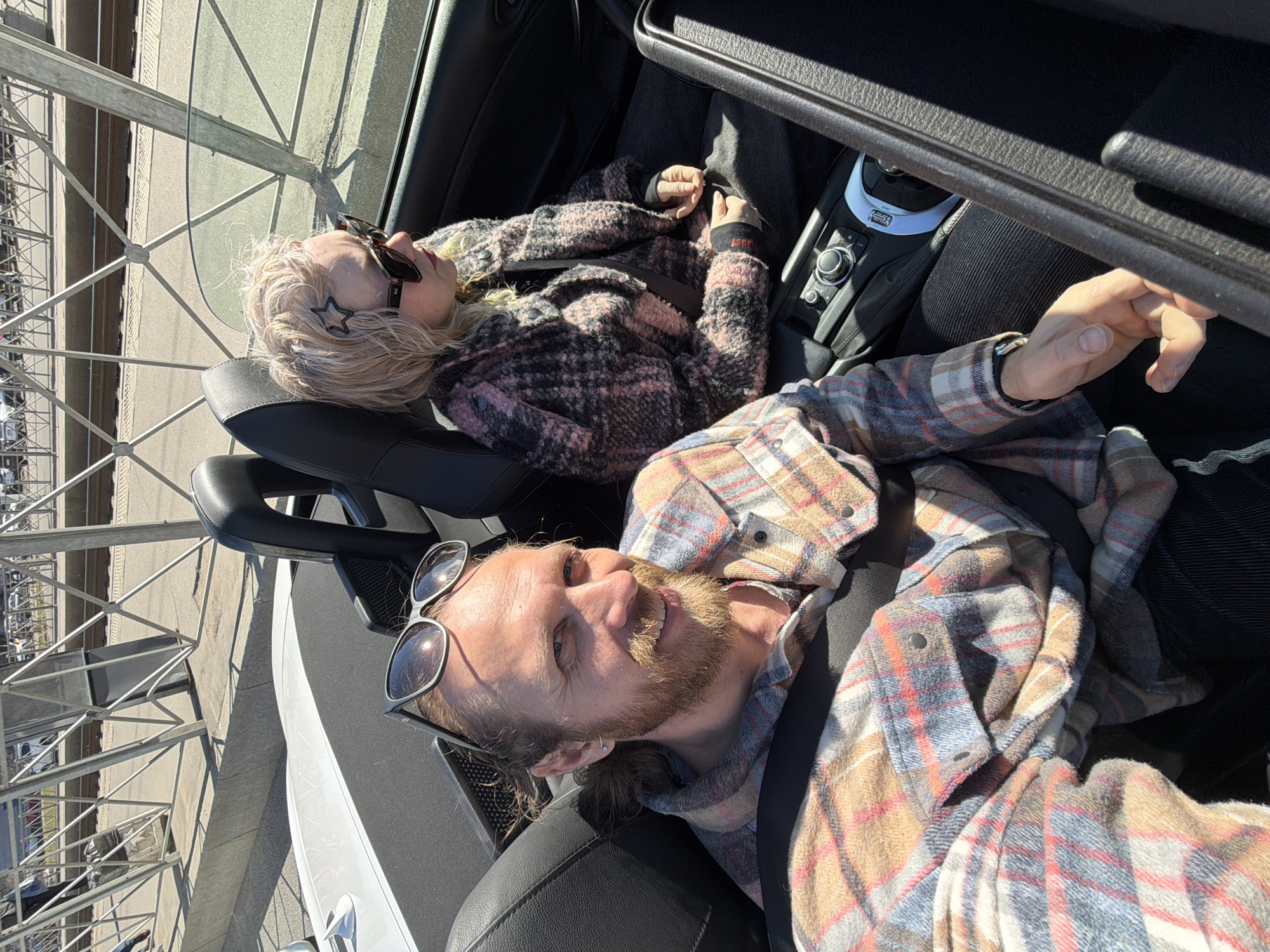 Two people enjoy sunny day in convertible near structure