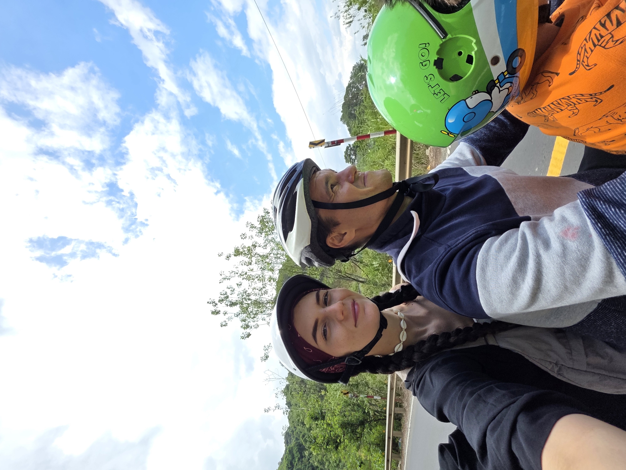 Three helmet-wearing riders travel mountain road in rural Vietnam