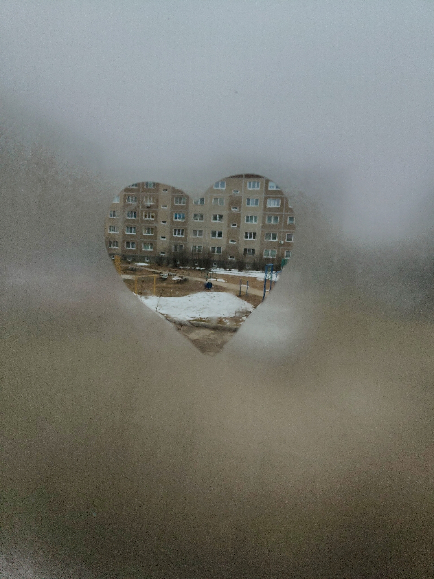 Heart traced in window condensation frames apartment building view
