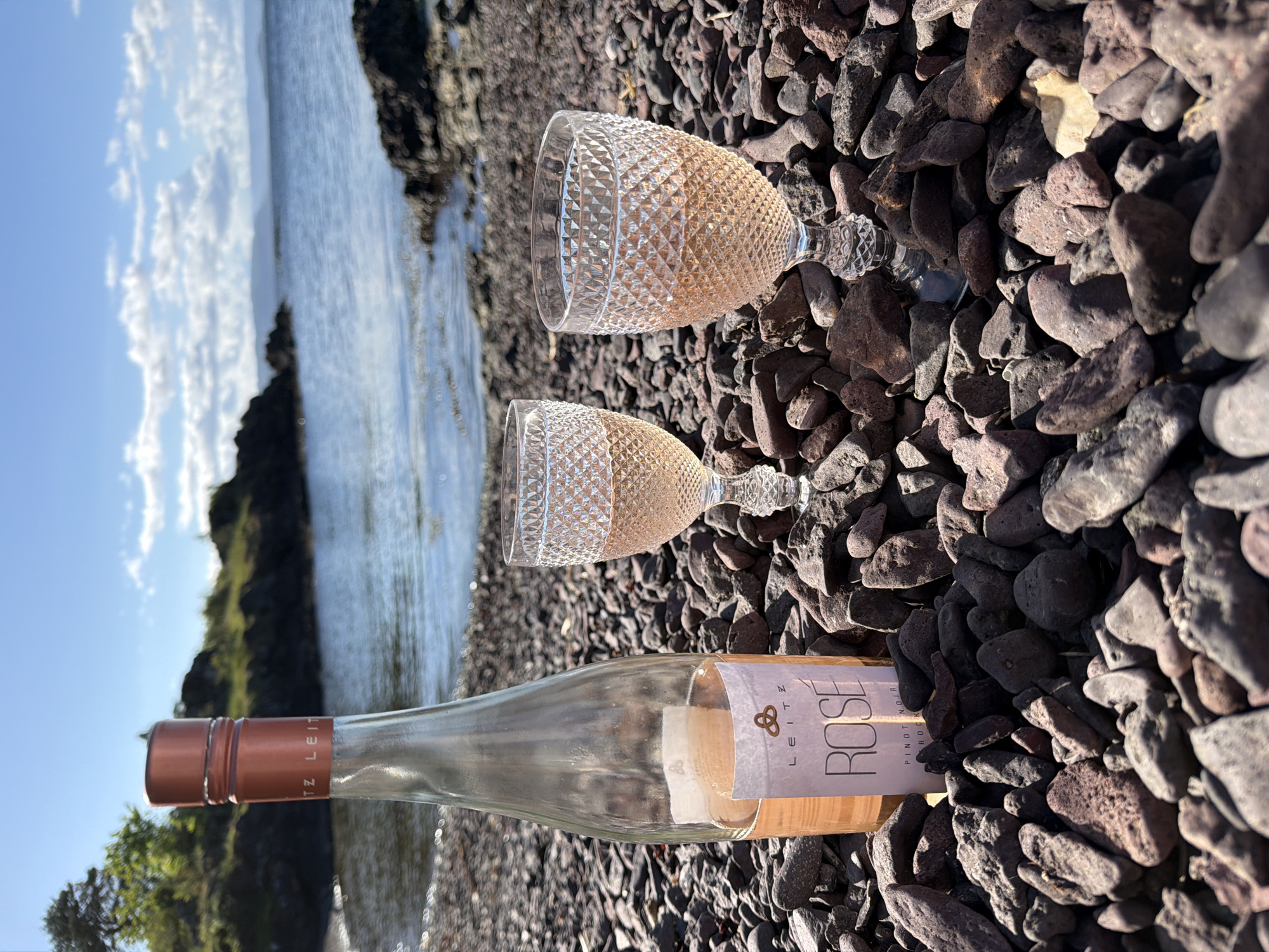 Rosé wine glasses rest on stone shoreline in Norway