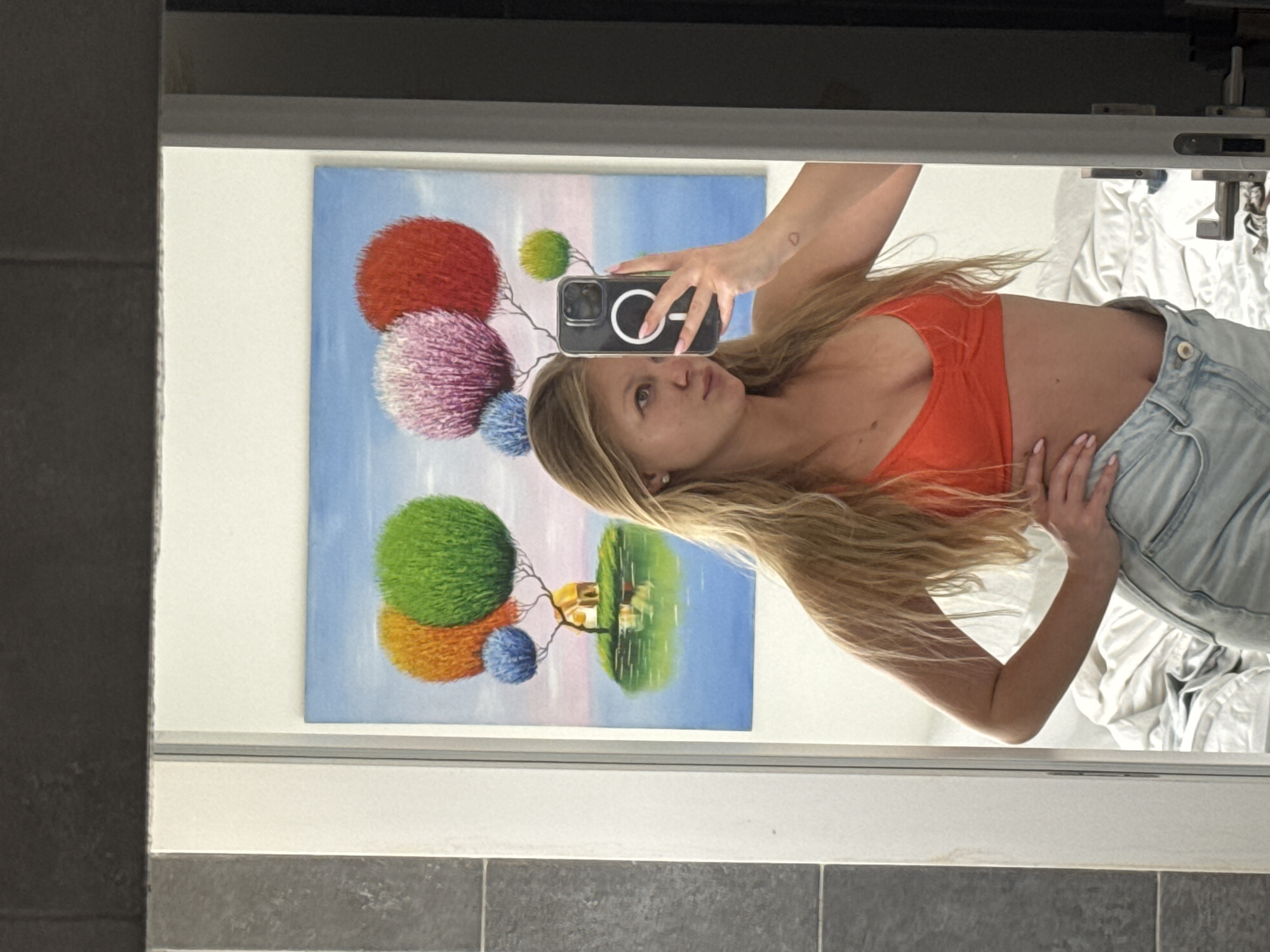 Woman takes mirror selfie in orange top in Ariel