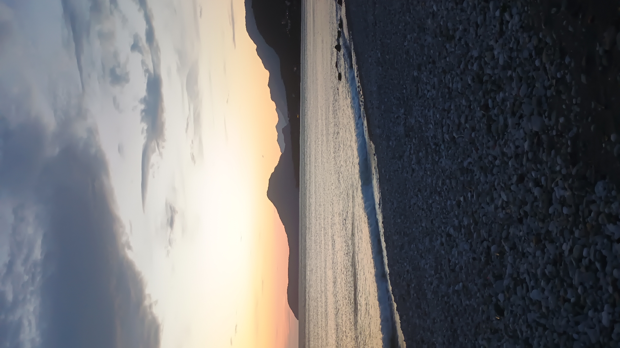 Sunset transforms rocky beach sky from gray to orange