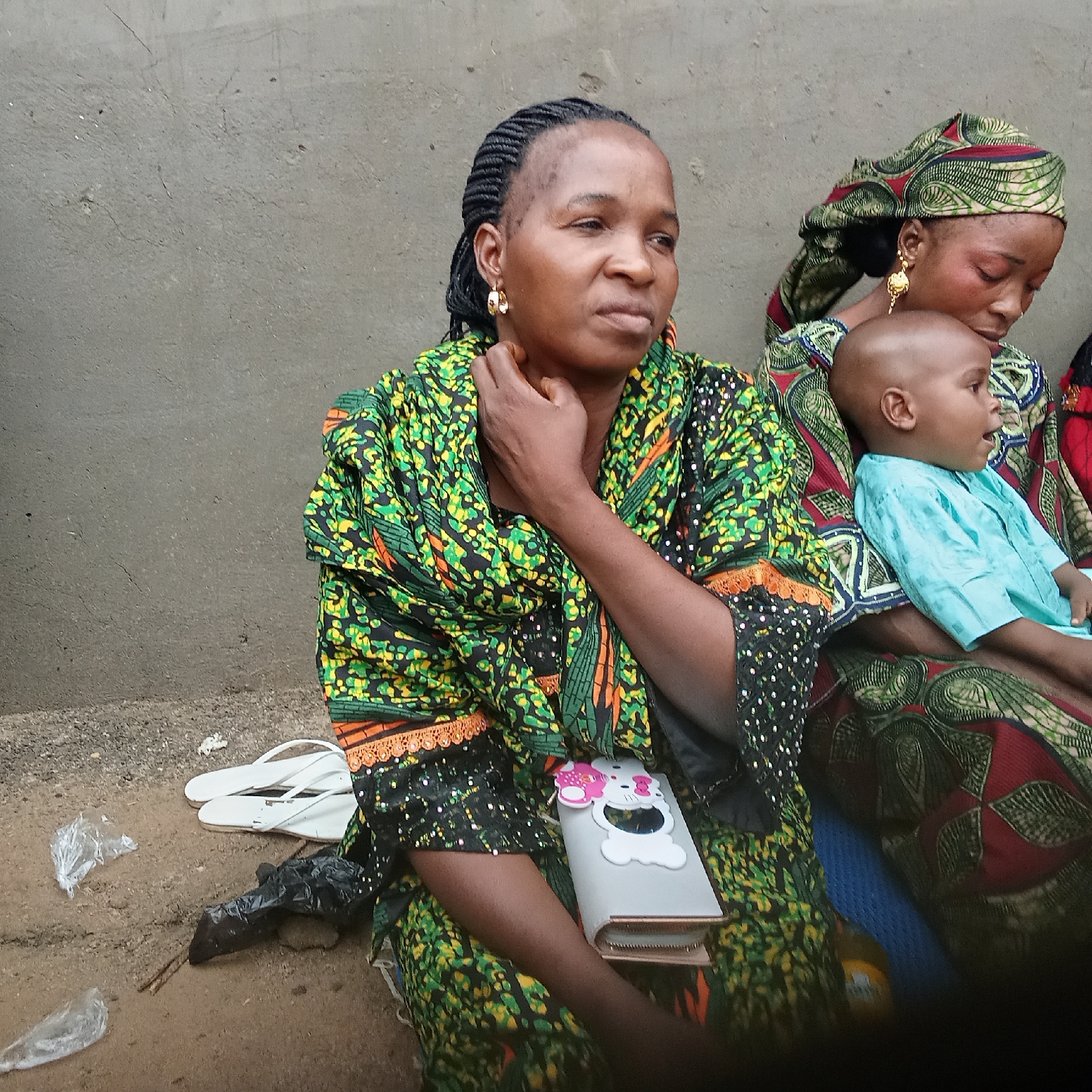 Women and child gather outside concrete wall in Doma
