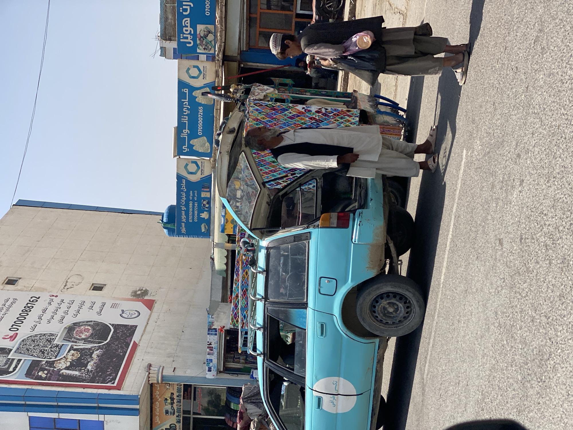 Colorful textile goods on display from a parked station wagon in Kandahar