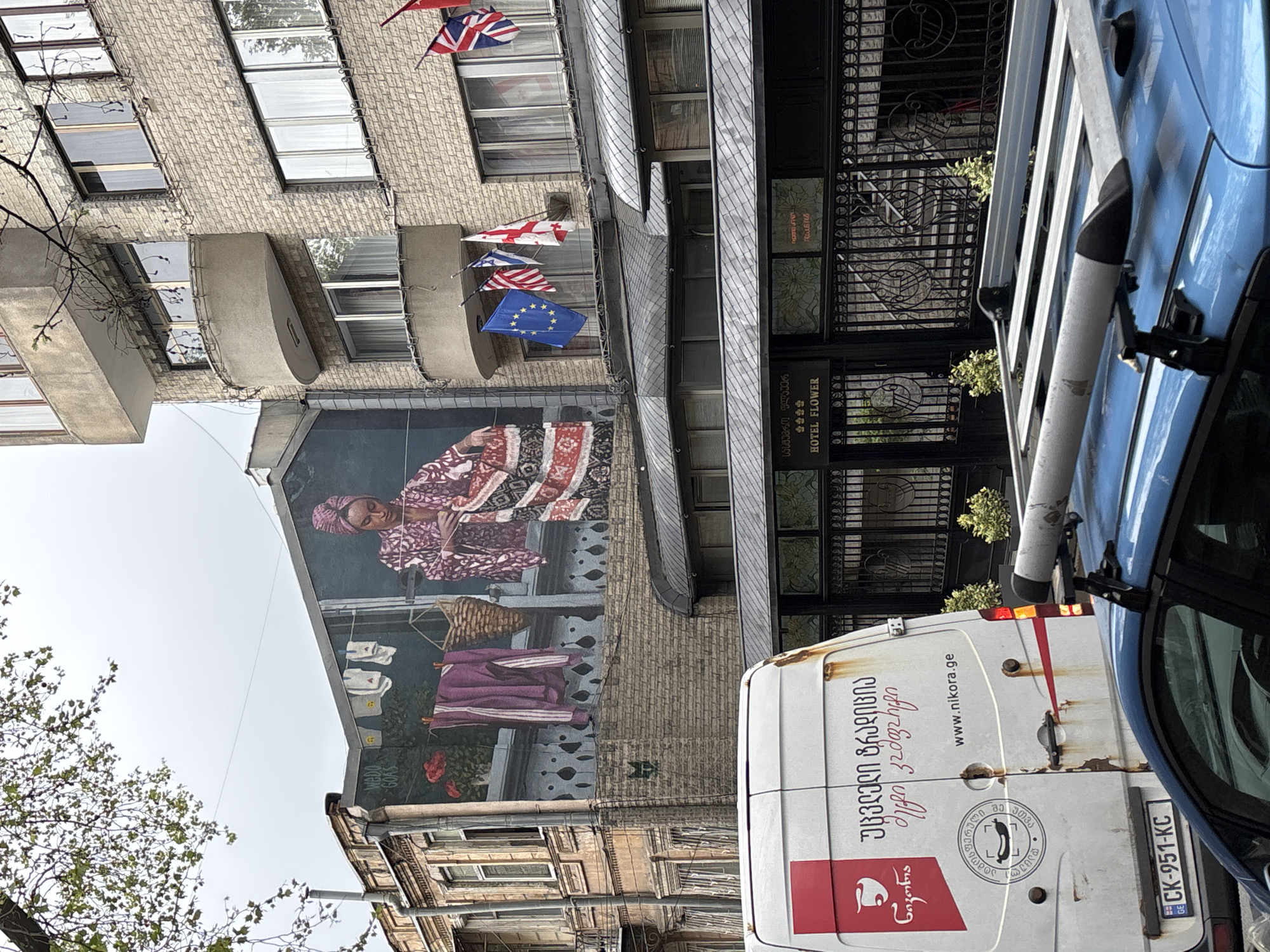 Traditional woman mural spotted on Tbilisi street with flags