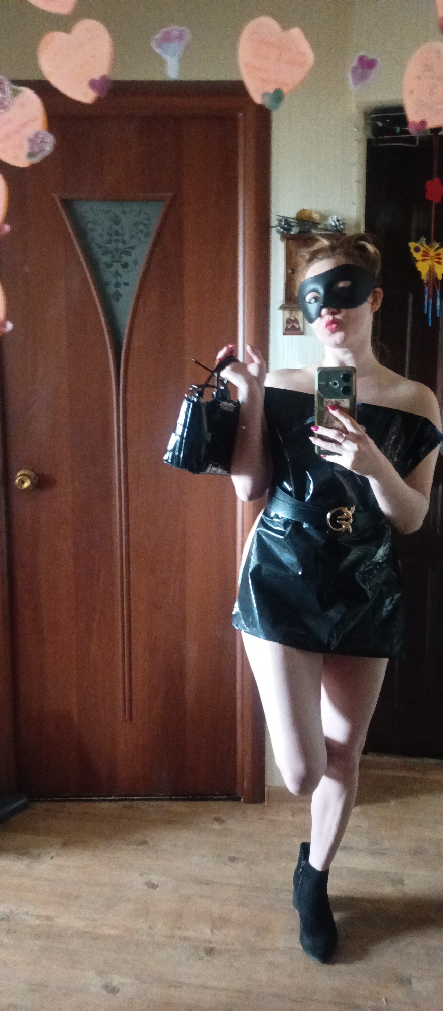 Masked woman in black dress takes mirror selfies indoors
