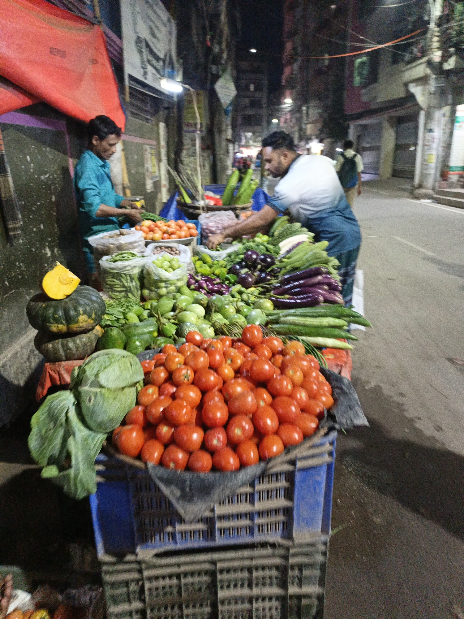 Evening vegetable vendors work Dhaka streets near pharmacy