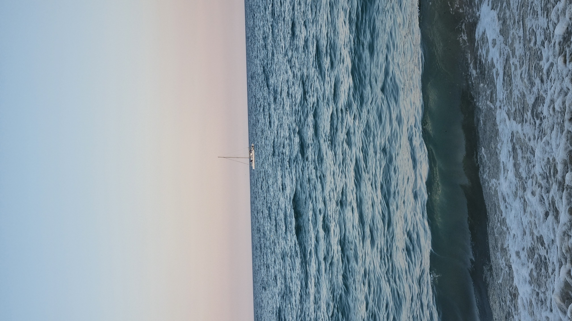 Motorcycle parked, beach nearly empty, sailboat on the horizon