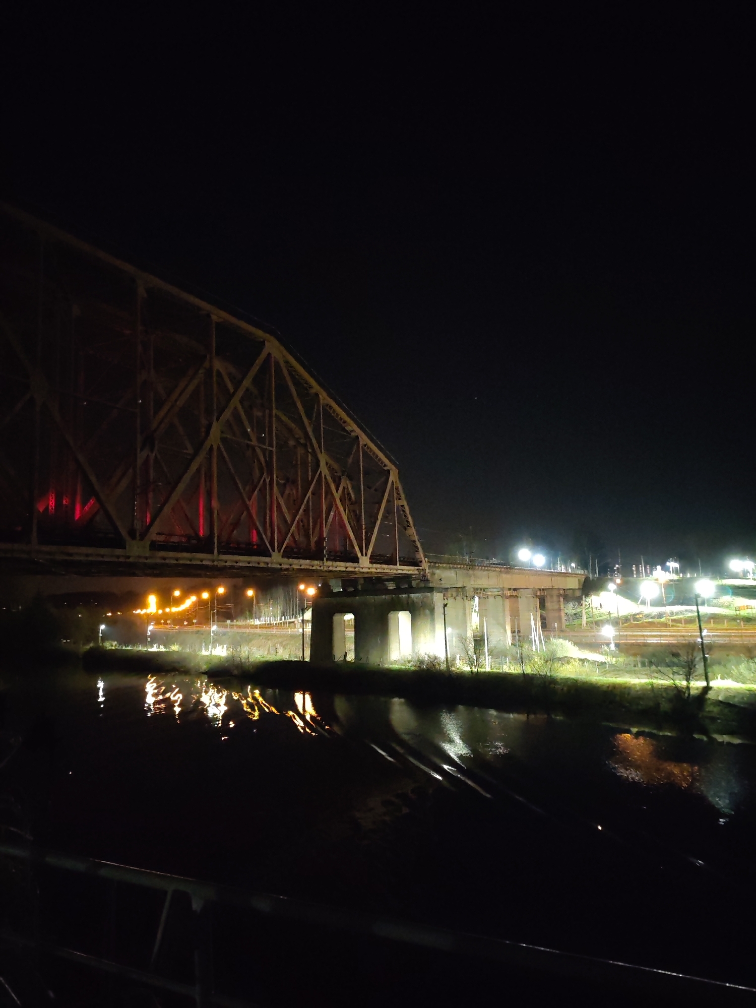 Illuminated bridge spans river in Dedenevo with vessel below