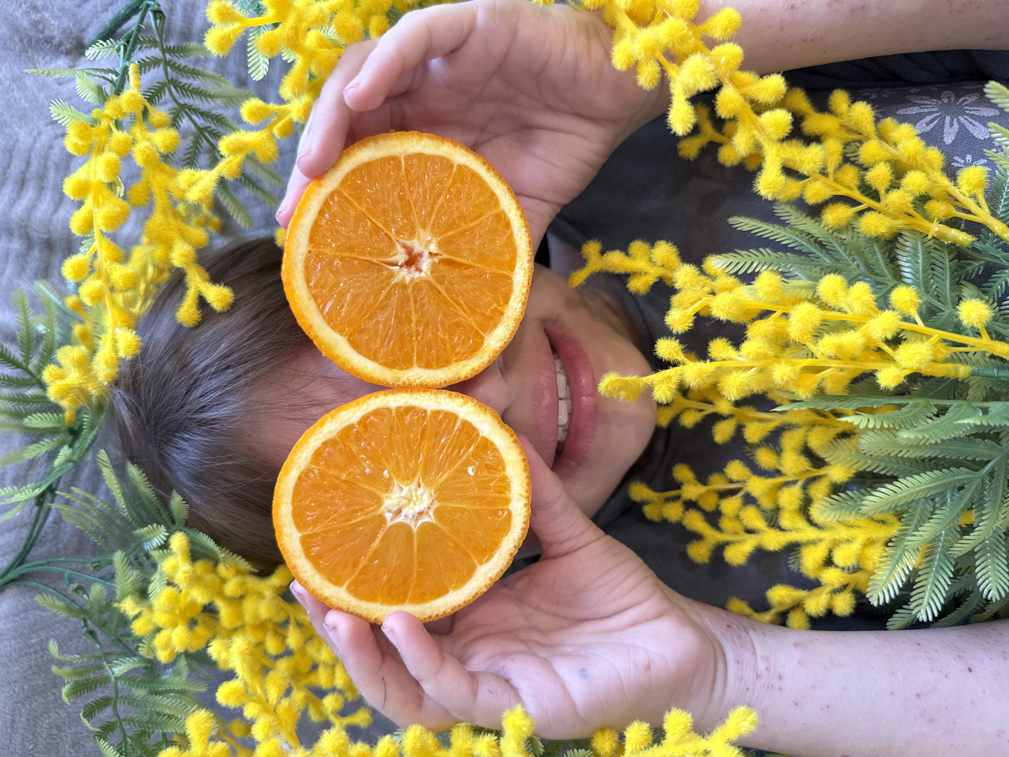 Person playfully poses with orange halves over eyes
