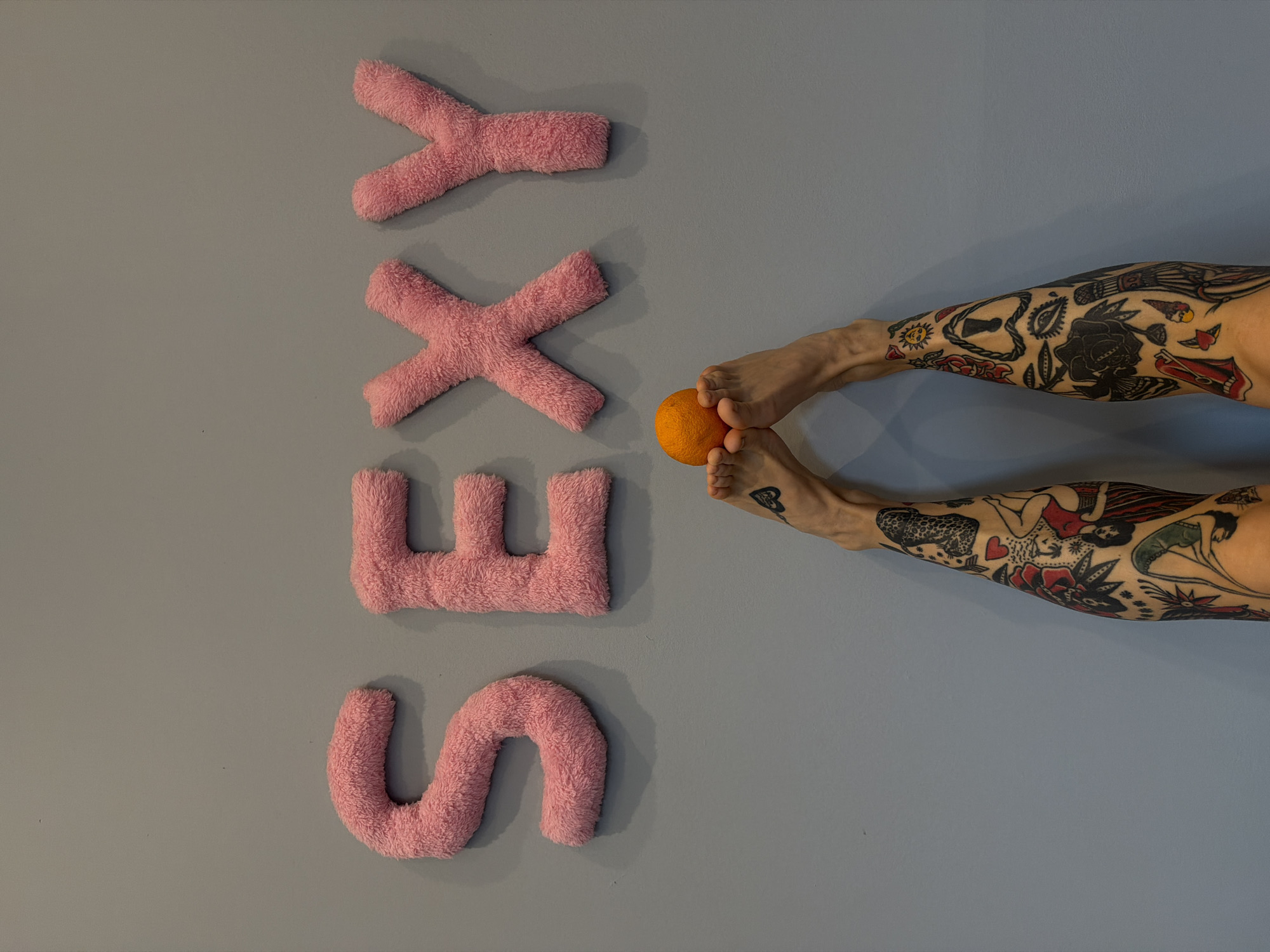Tattooed feet, gray wall, pink fuzzy letters spelling SEXY