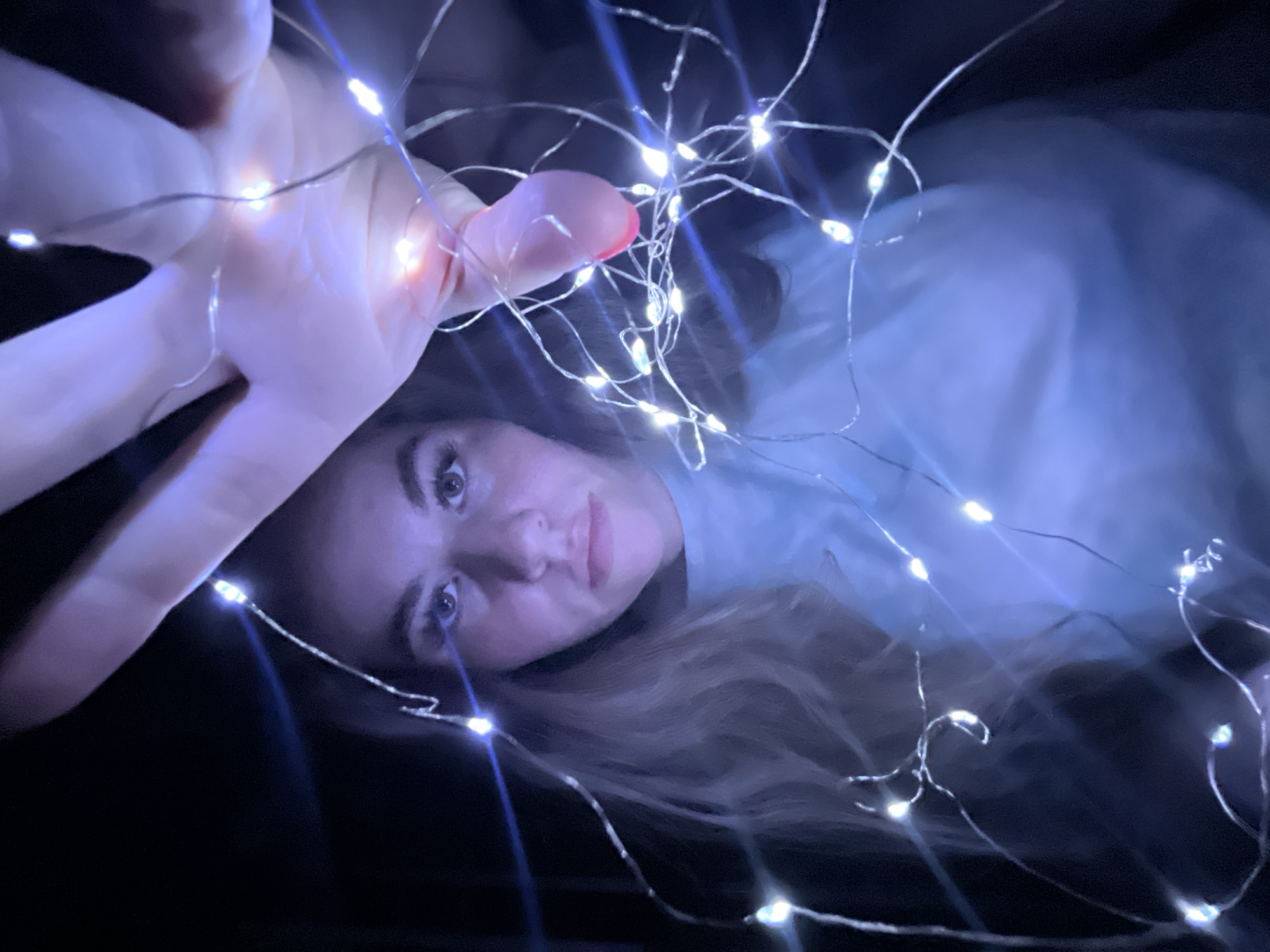 Woman poses with fairy lights in darkened space