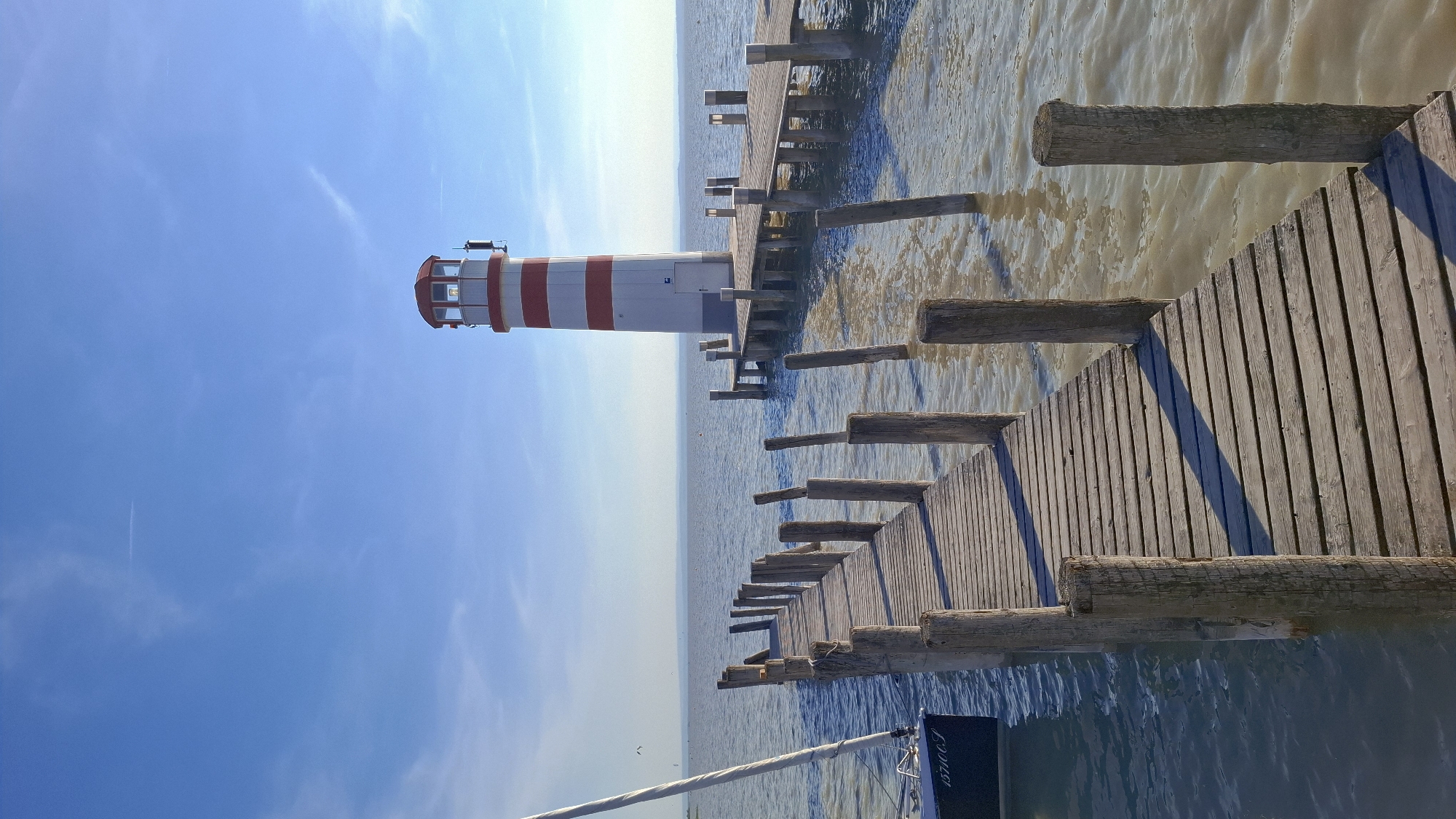 Striped lighthouse observed on wooden pier in Austrian lakeside town