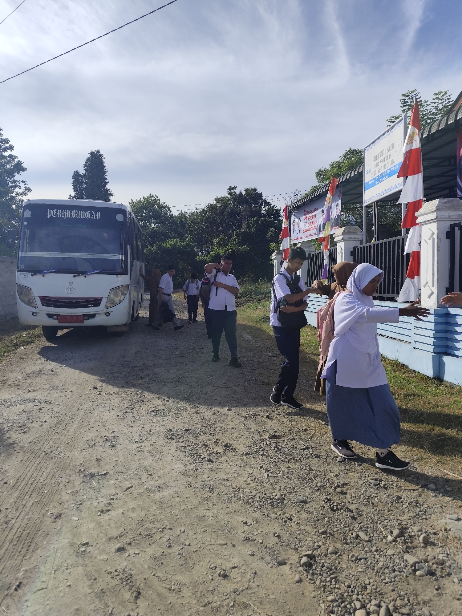 Students in uniform boarding a school bus on a dirt road