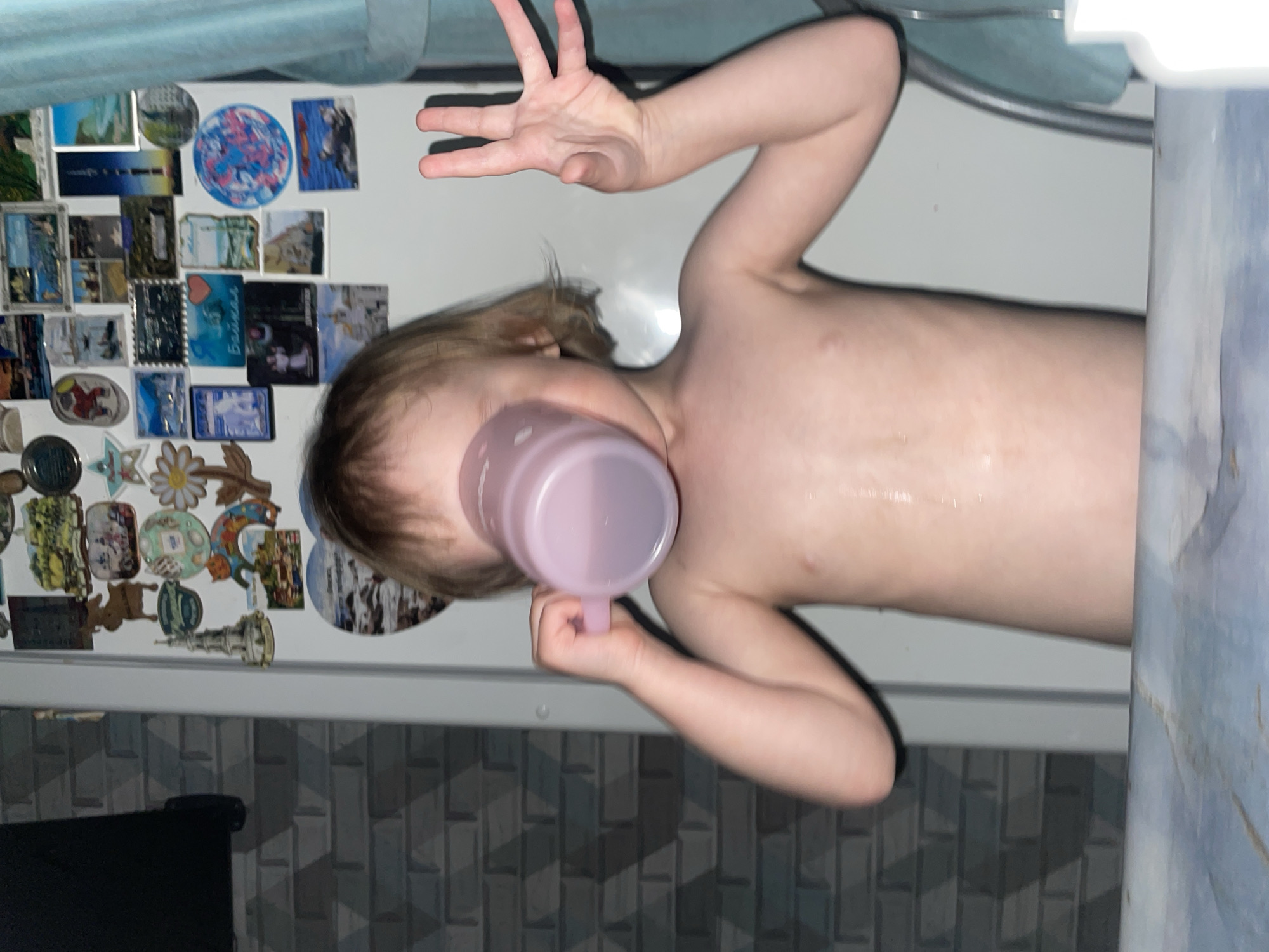 Child drinks from pink cup during bath time in Vladivostok
