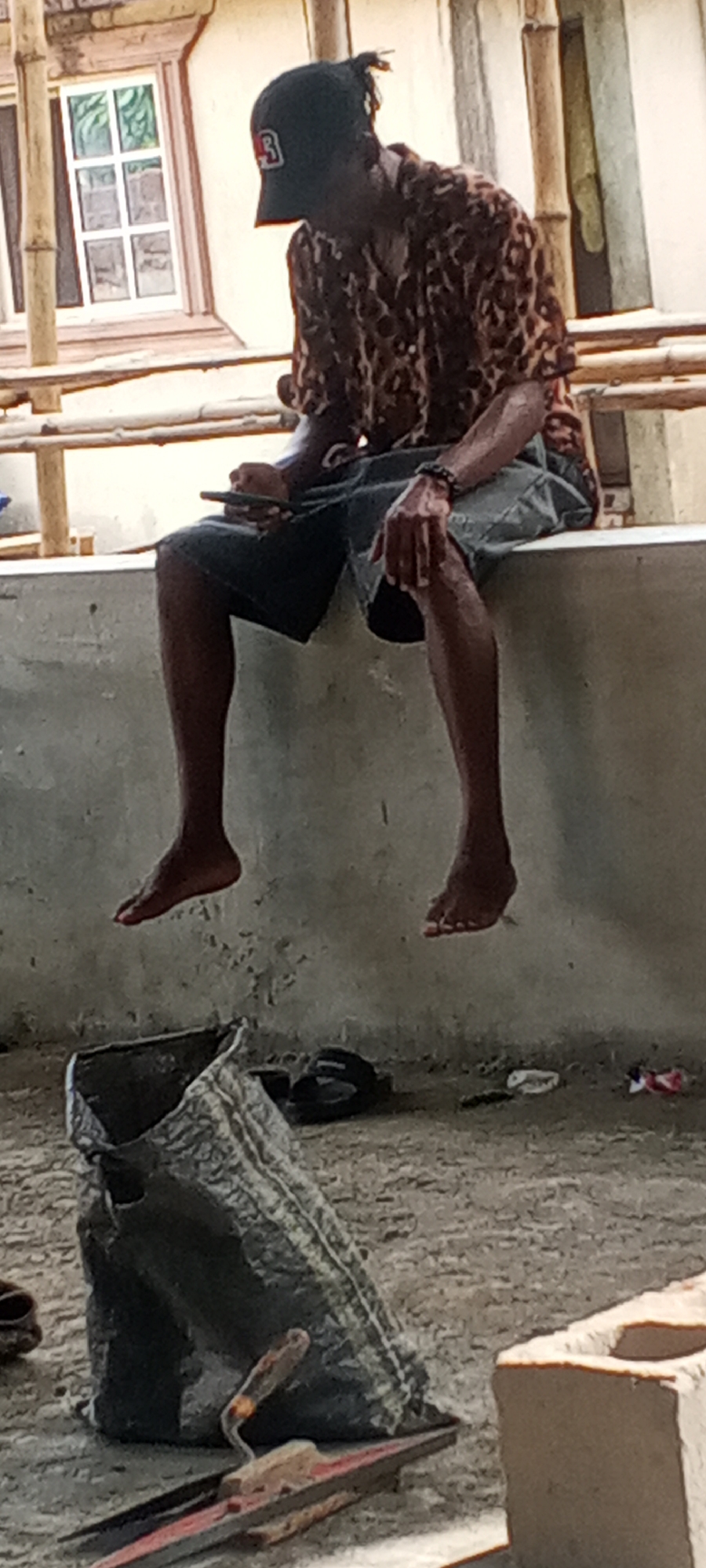 Person in leopard print shirt sits on ledge with phone