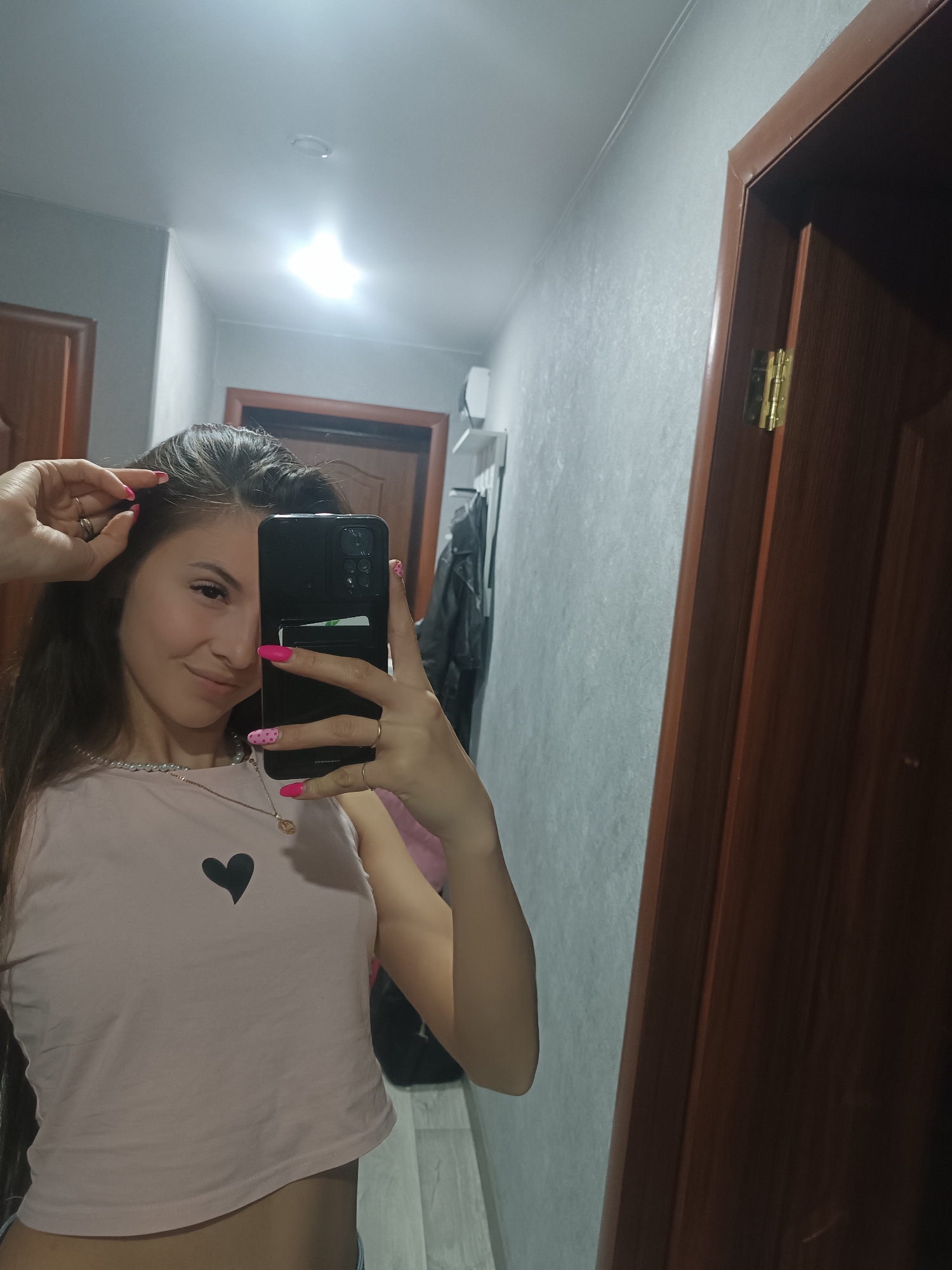Woman takes selfie in hallway wearing pink top