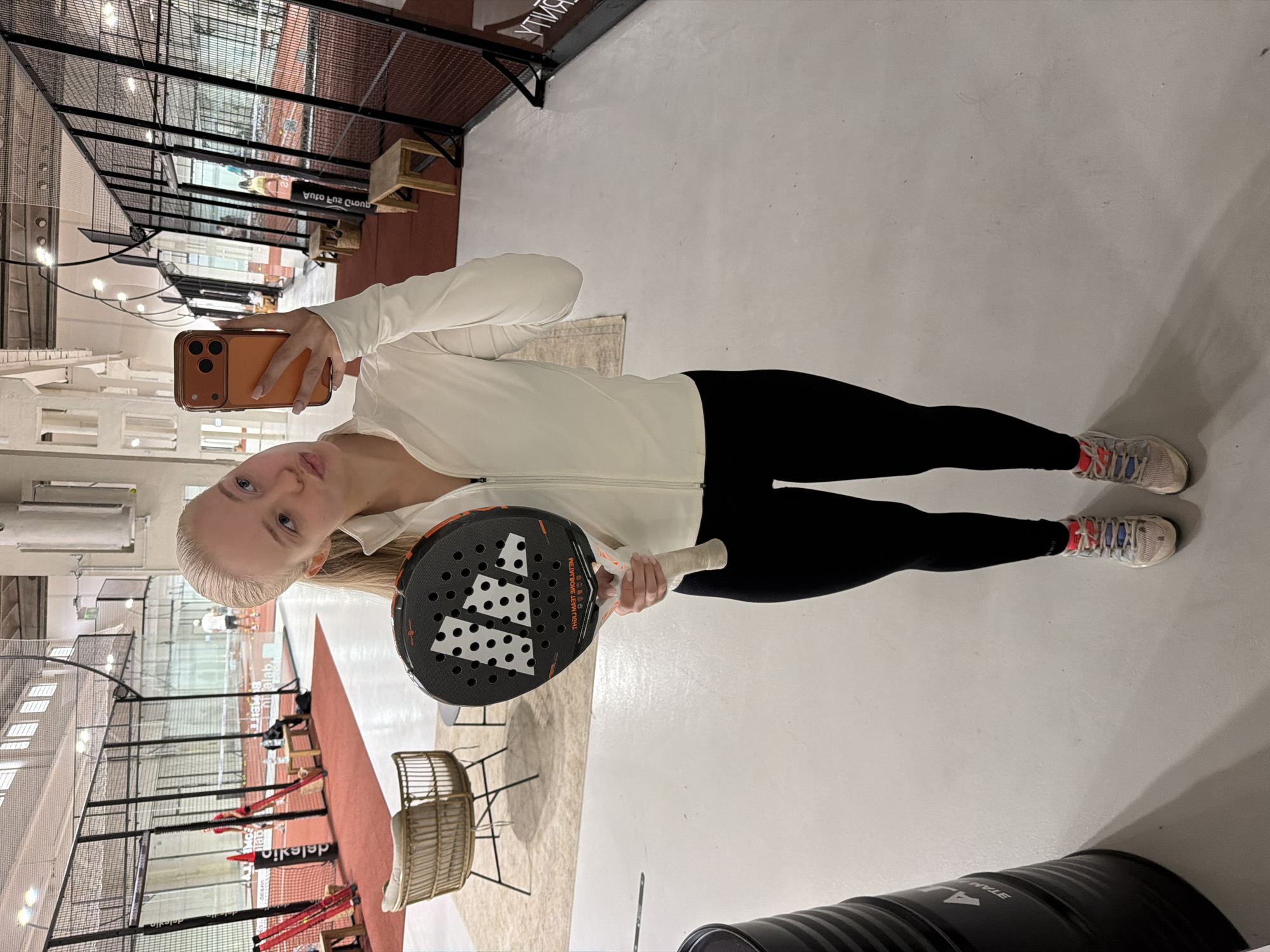 Woman takes selfies during padel tennis session at indoor facility