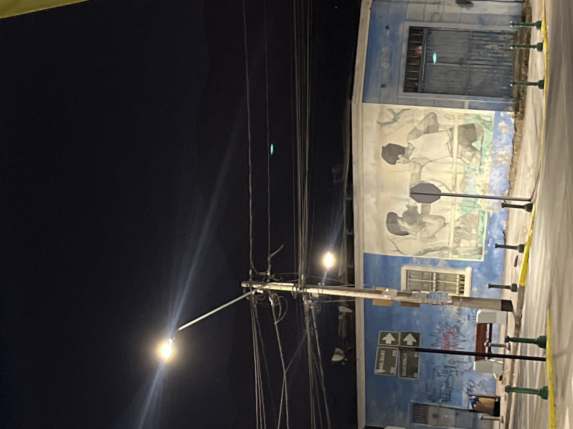 Nighttime street lamp illuminates building mural depicting human figures