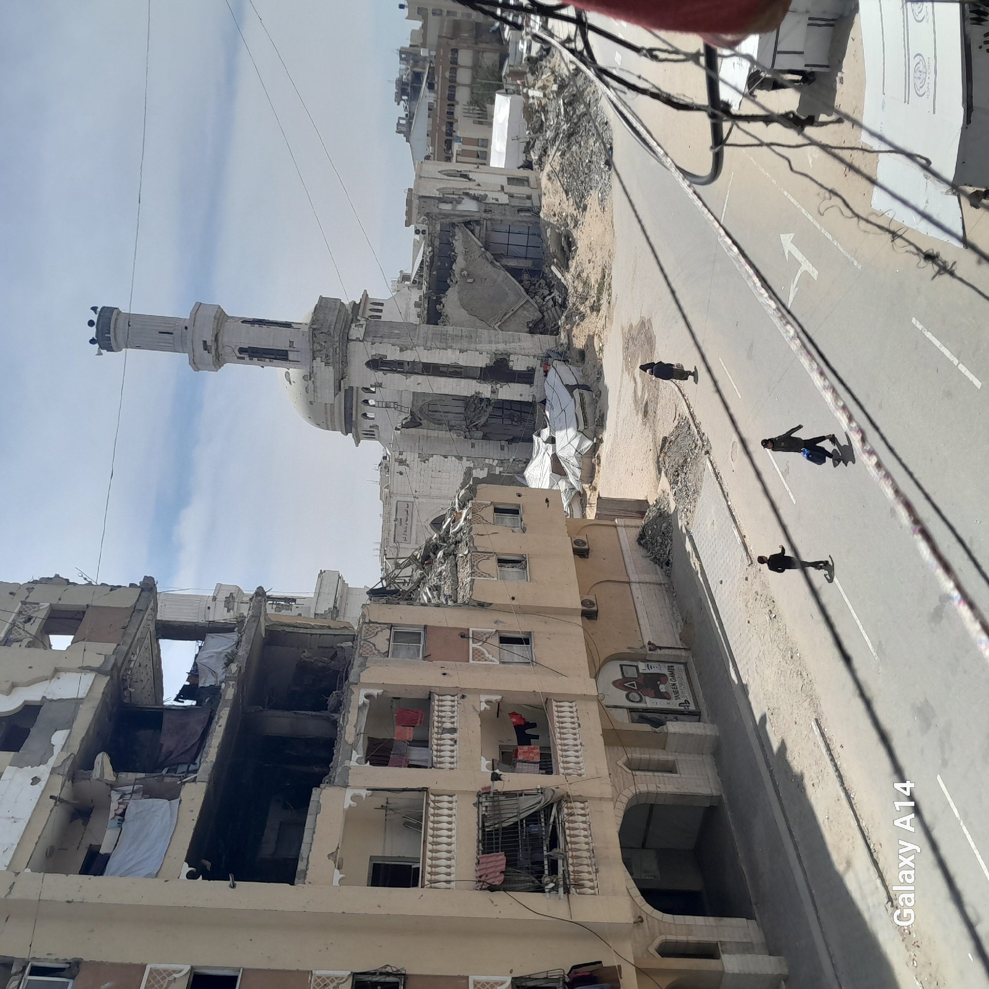 Urban street shows widespread building damage including mosque