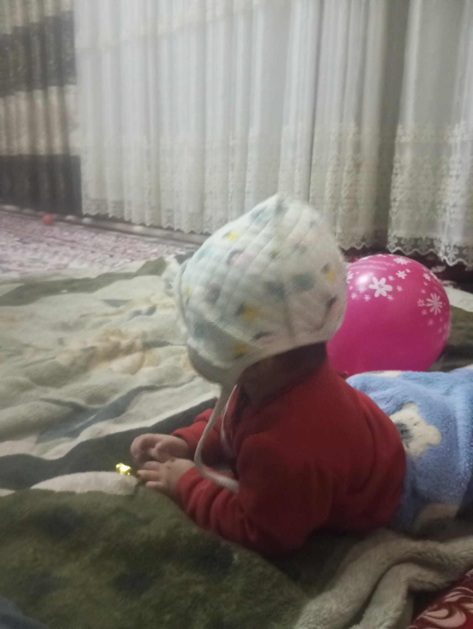 Child with pink balloon sits on blanket outdoors
