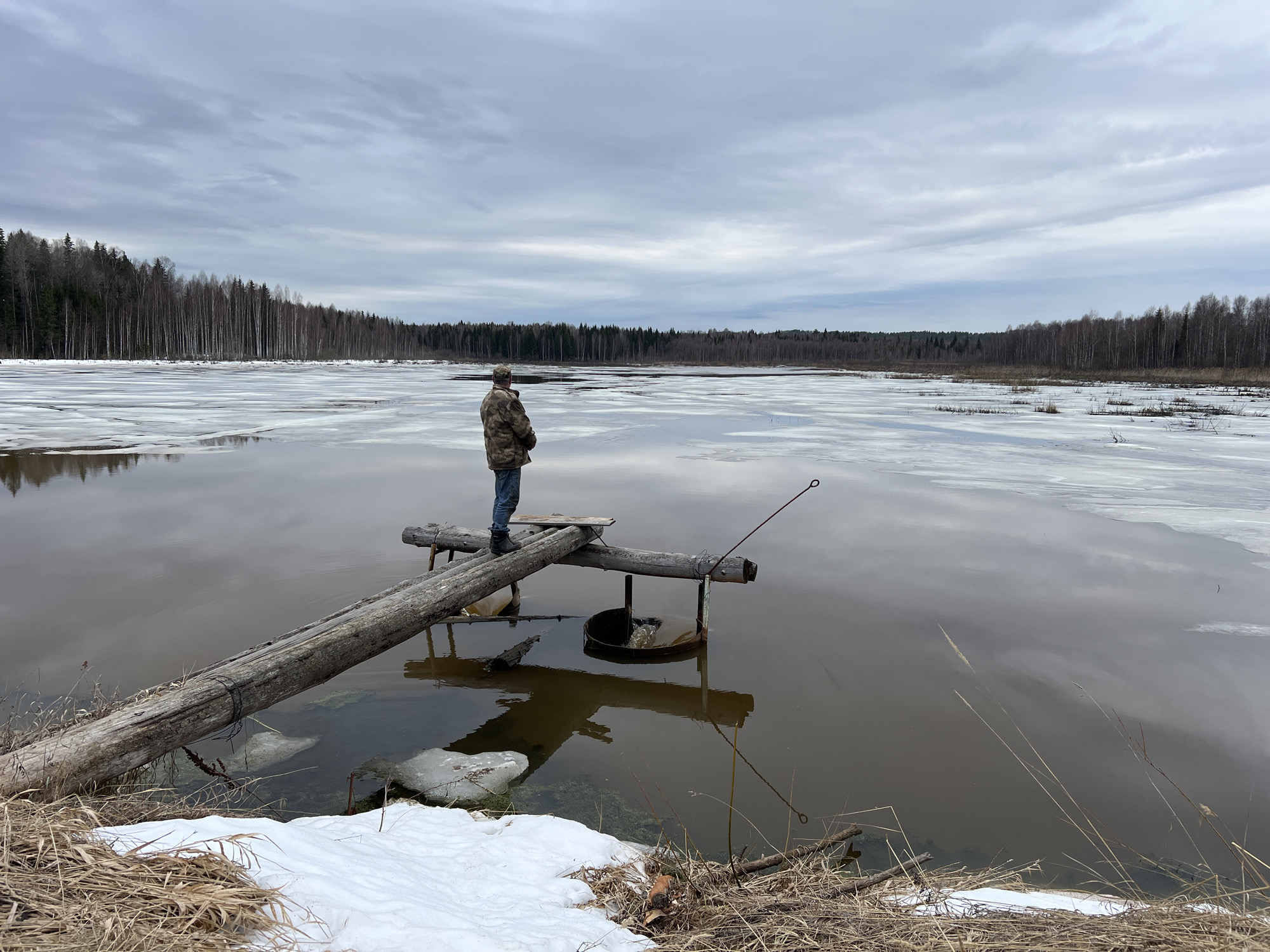 Man stands on wooden pier in partially frozen waters, Posha