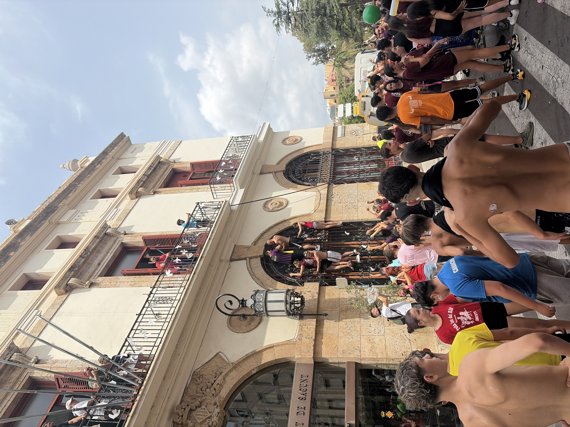 Crowds scale ornate building facade in Sagunto street scene