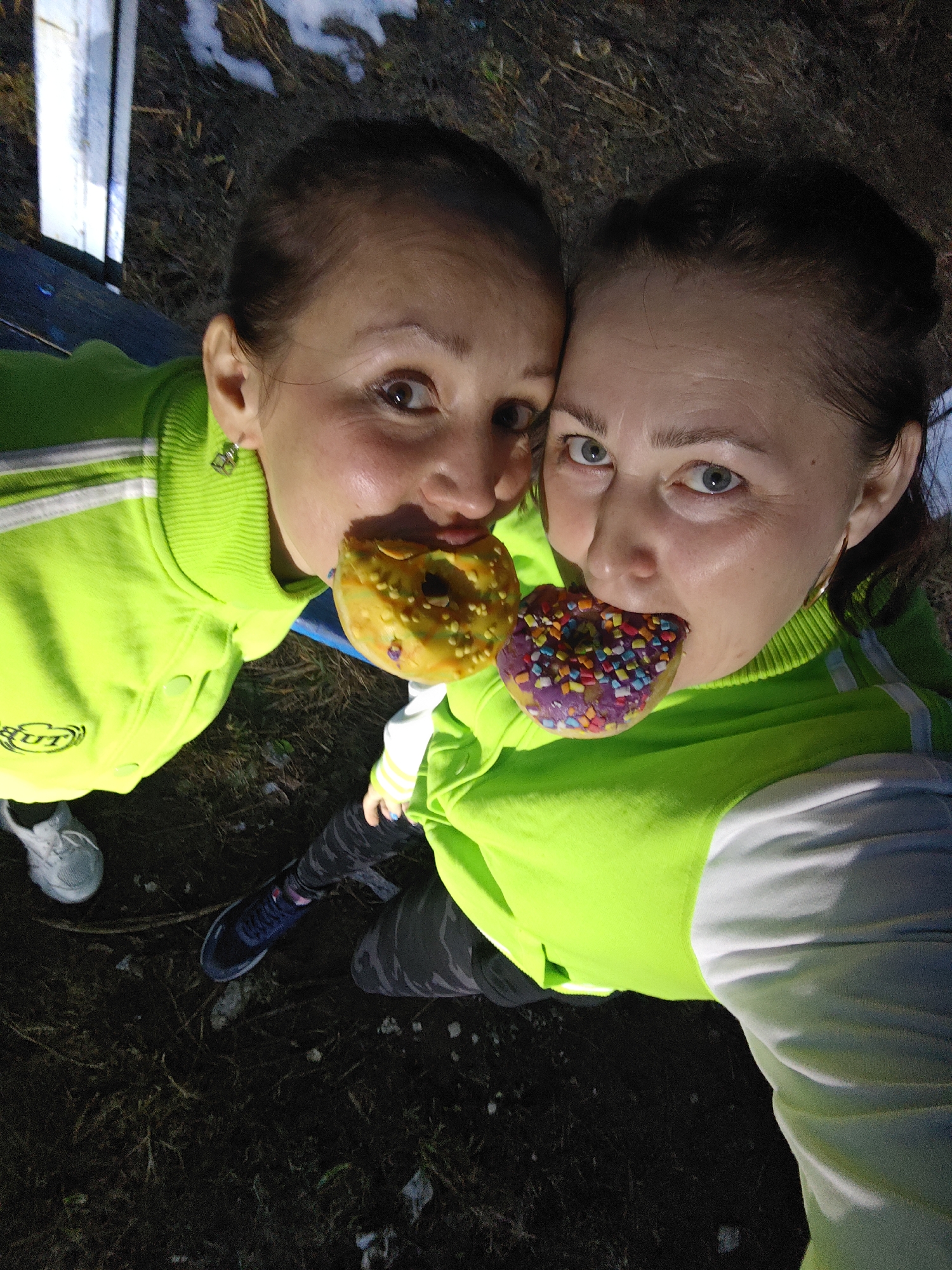 Two women share donuts outdoors in matching jackets
