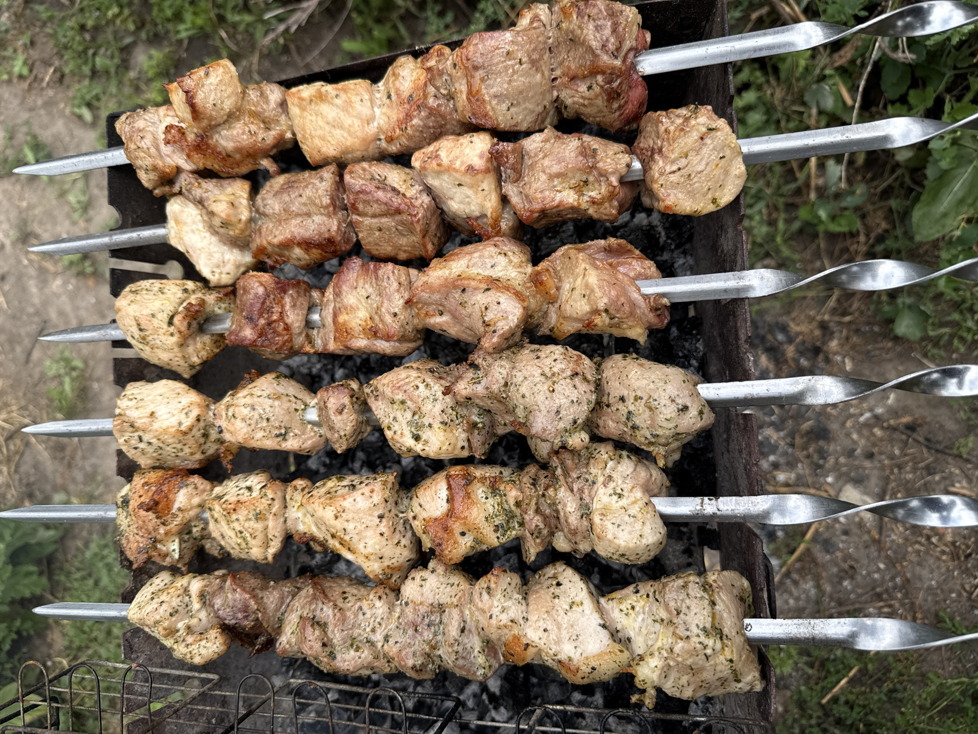 Charcoal grill loaded with skewers and bacon-wrapped meat outdoors