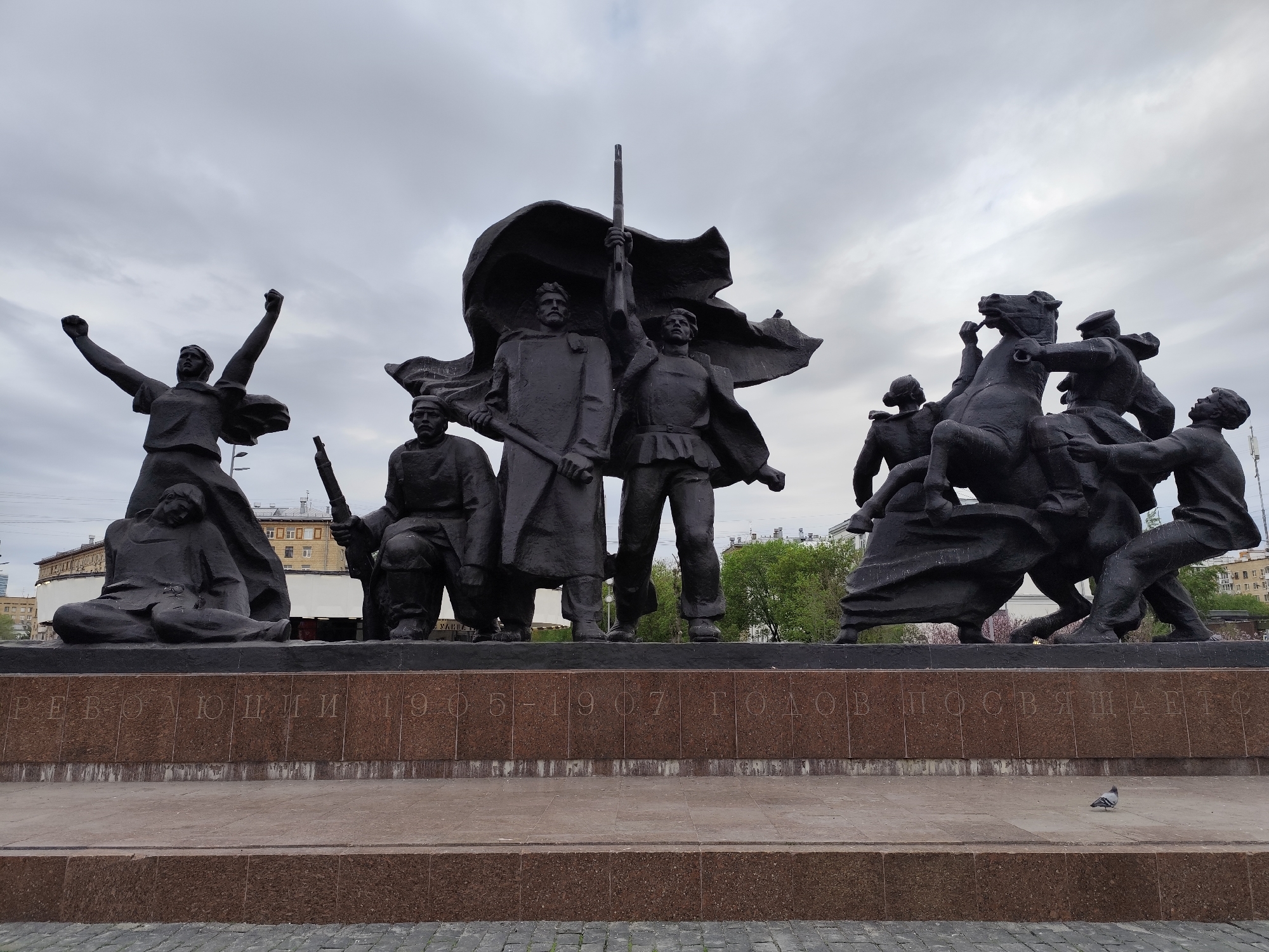 Bronze monument with multiple figures observed under grey skies