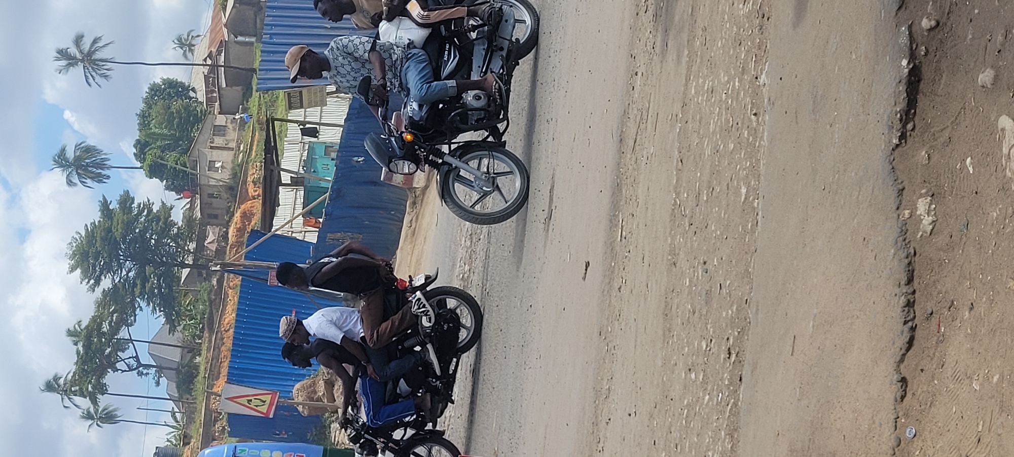 Motorcycles navigate a dusty Dar es Salaam street on a cloudy day