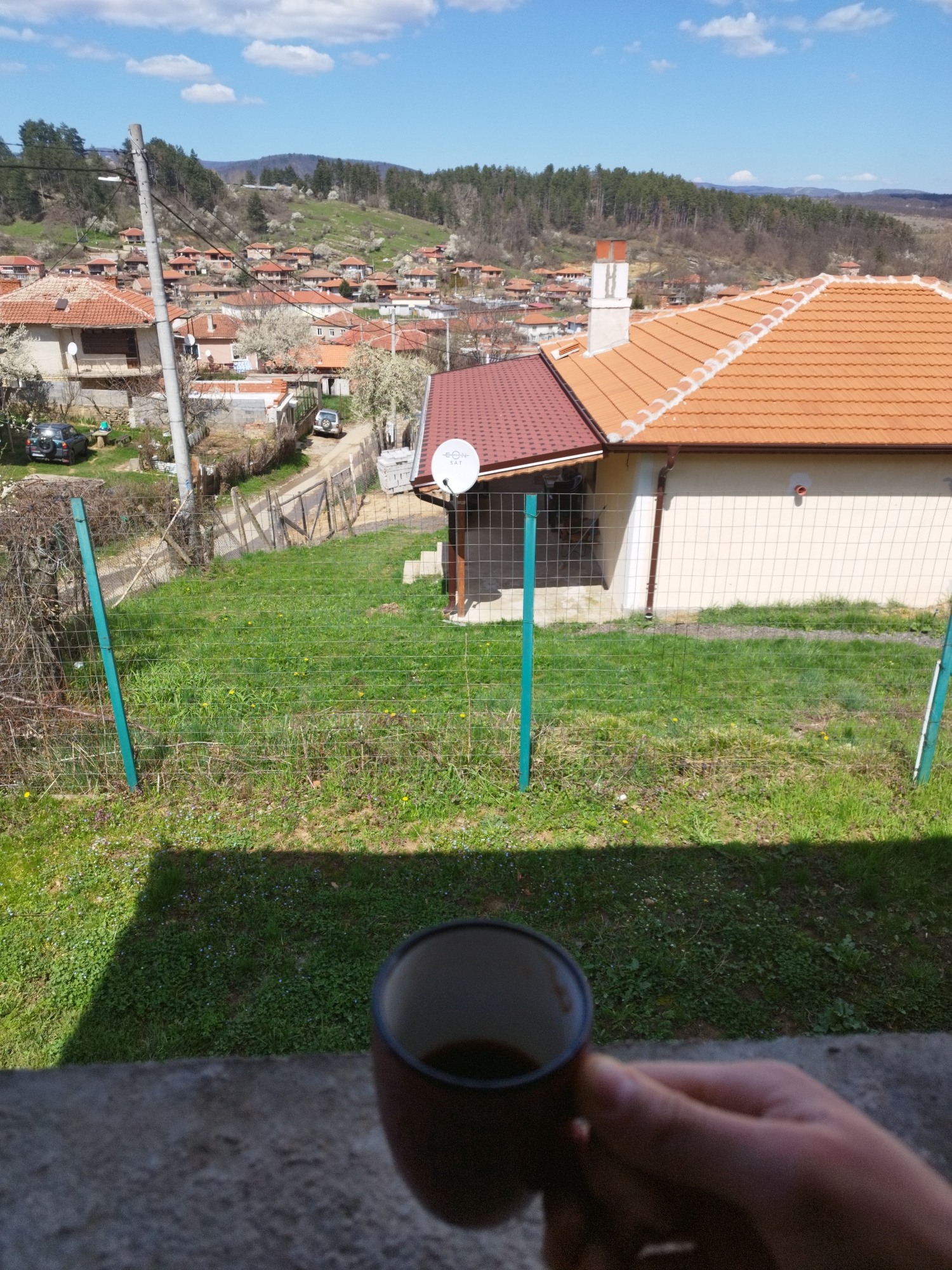 Person enjoys morning coffee overlooking rural landscape from balcony
