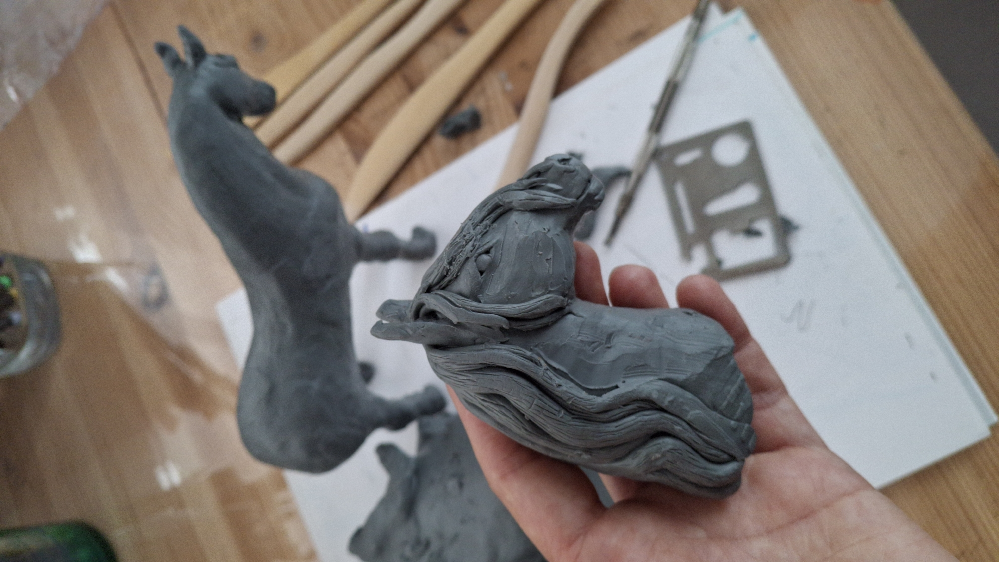 Artist sculpts clay horses in Russian studio, child plays nearby