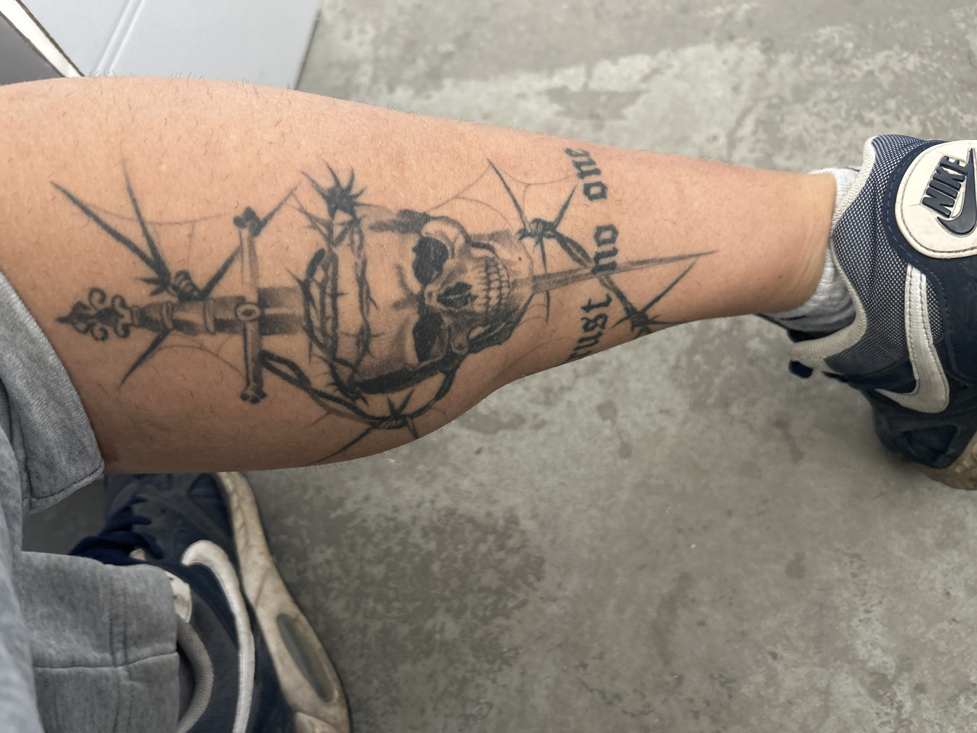 Person displays skull and sword tattoo with "trust no one" text