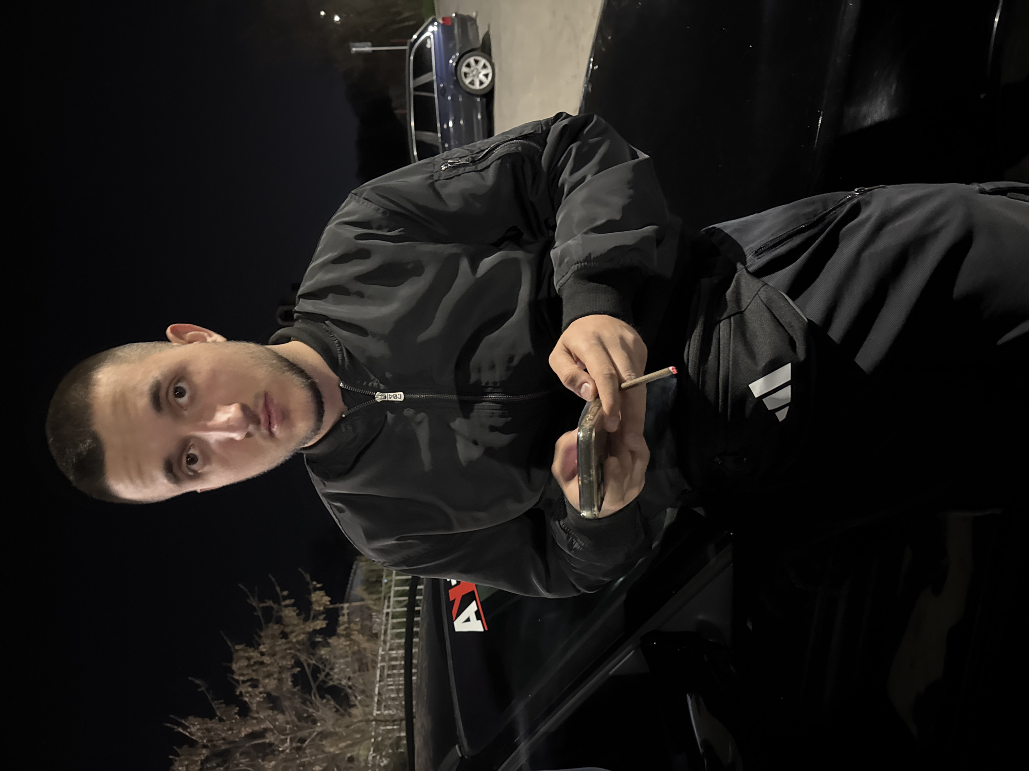 Young man with cigarette and phone leans against car in Topoli