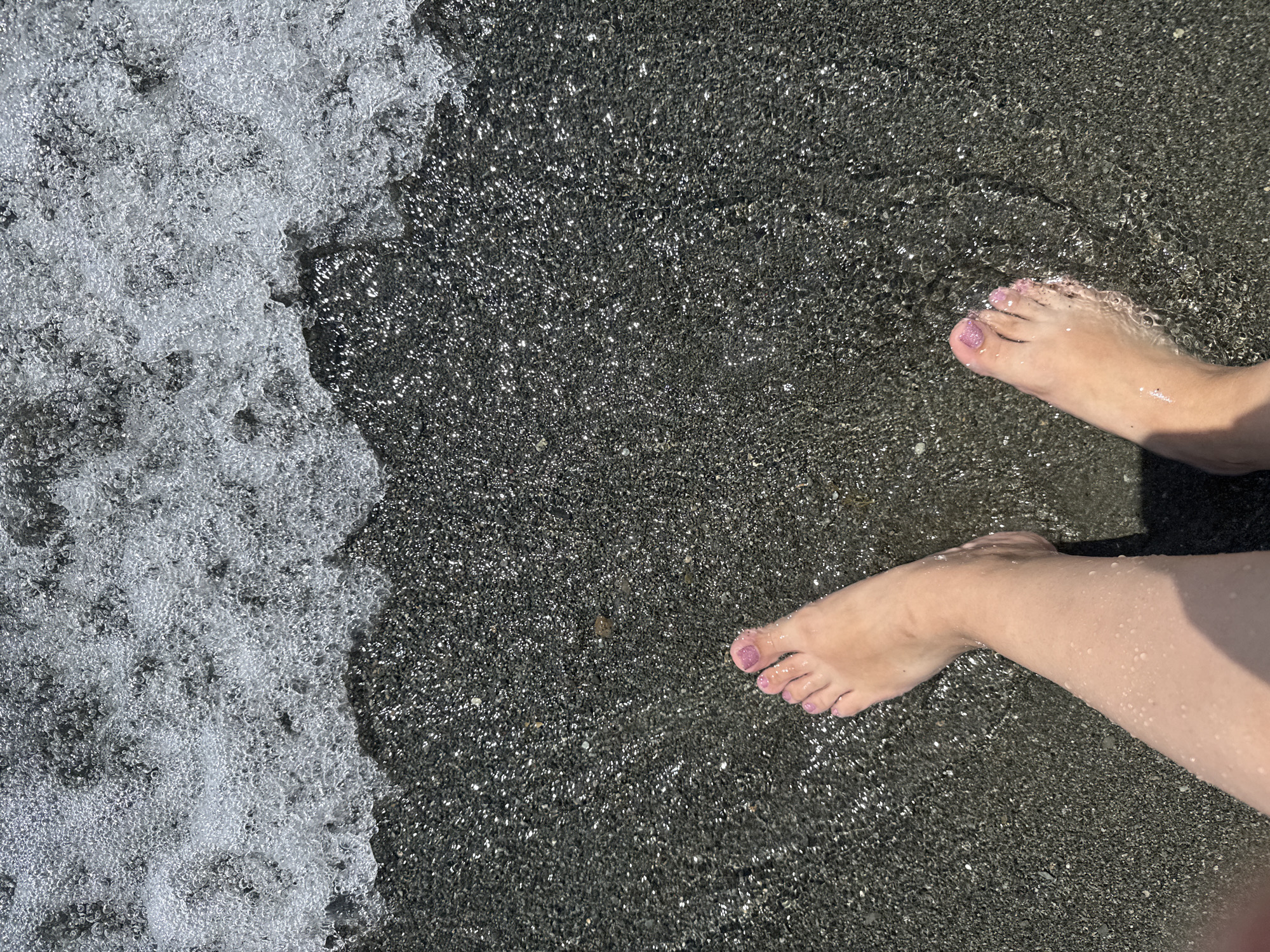 Wading the dark pebble shore of a lake in Armenia