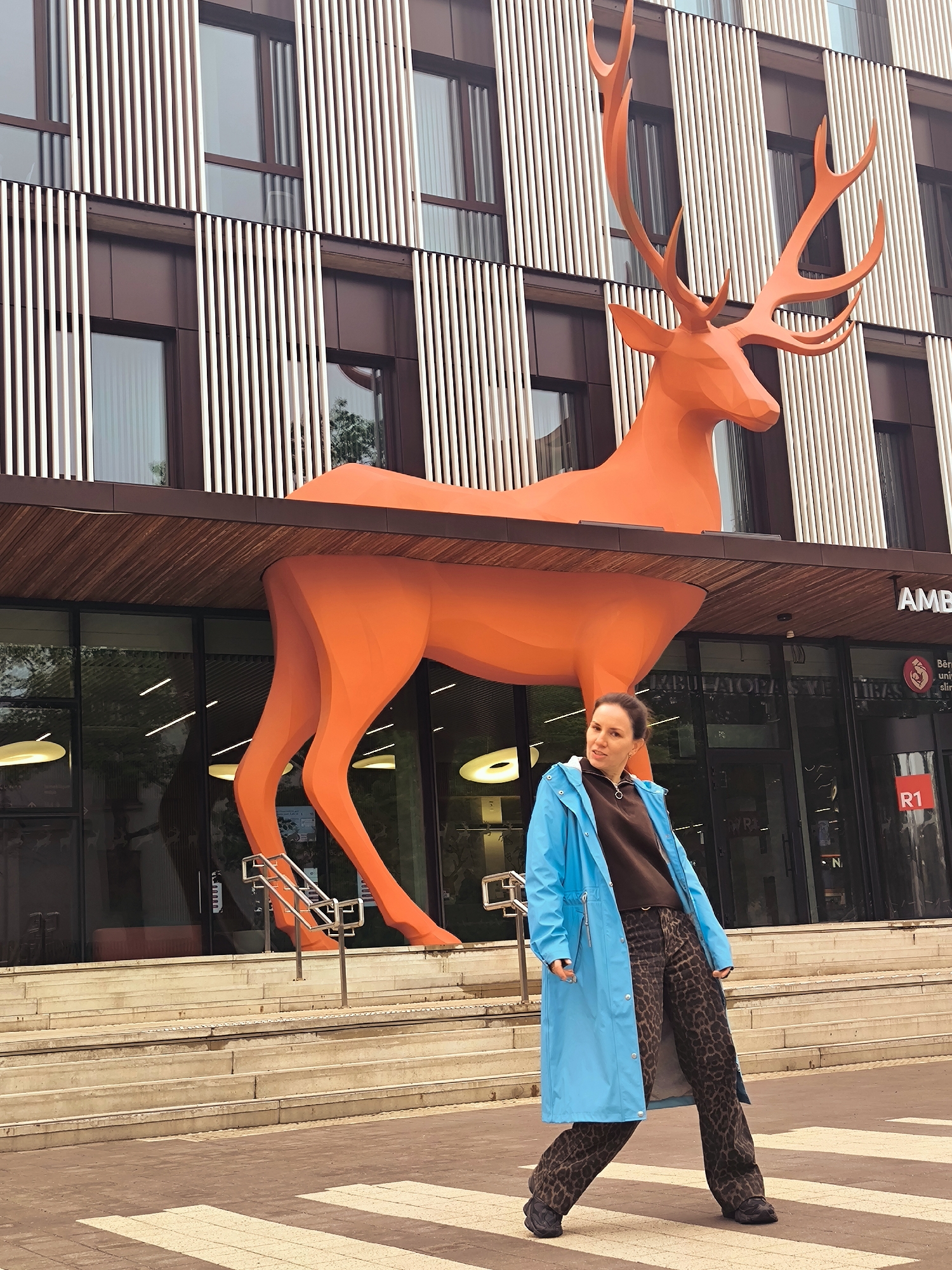 Woman photographed at Riga building with orange deer sculpture